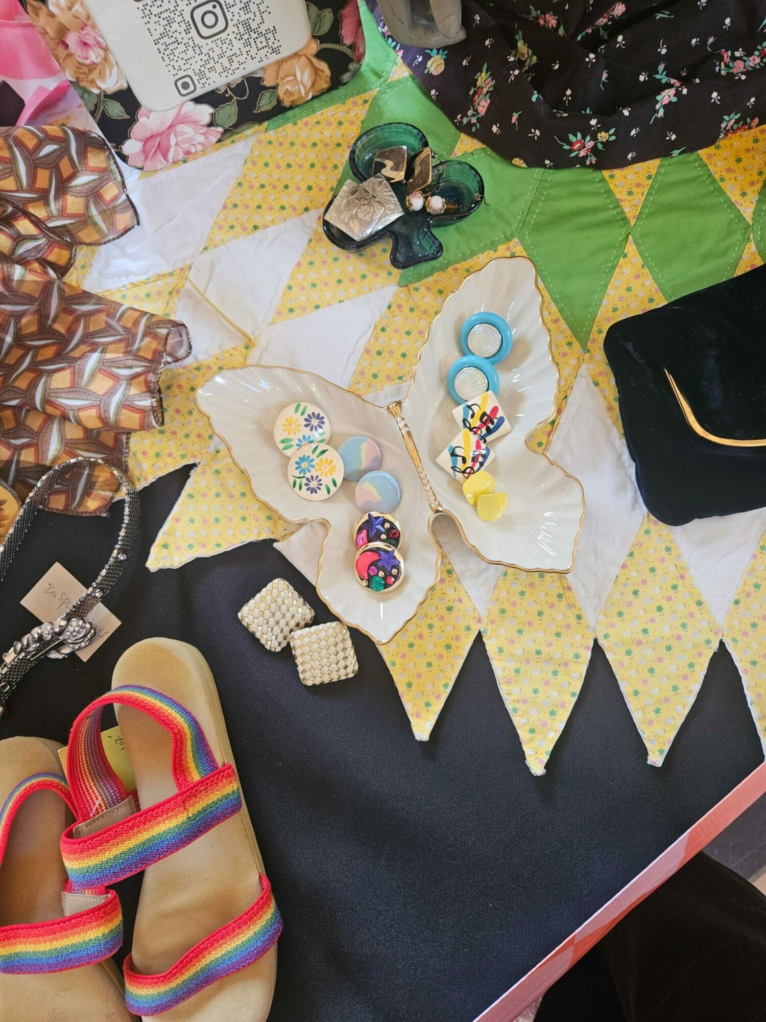 Colorful jewelry and accessories displayed on a patterned fabric surface with various items around.