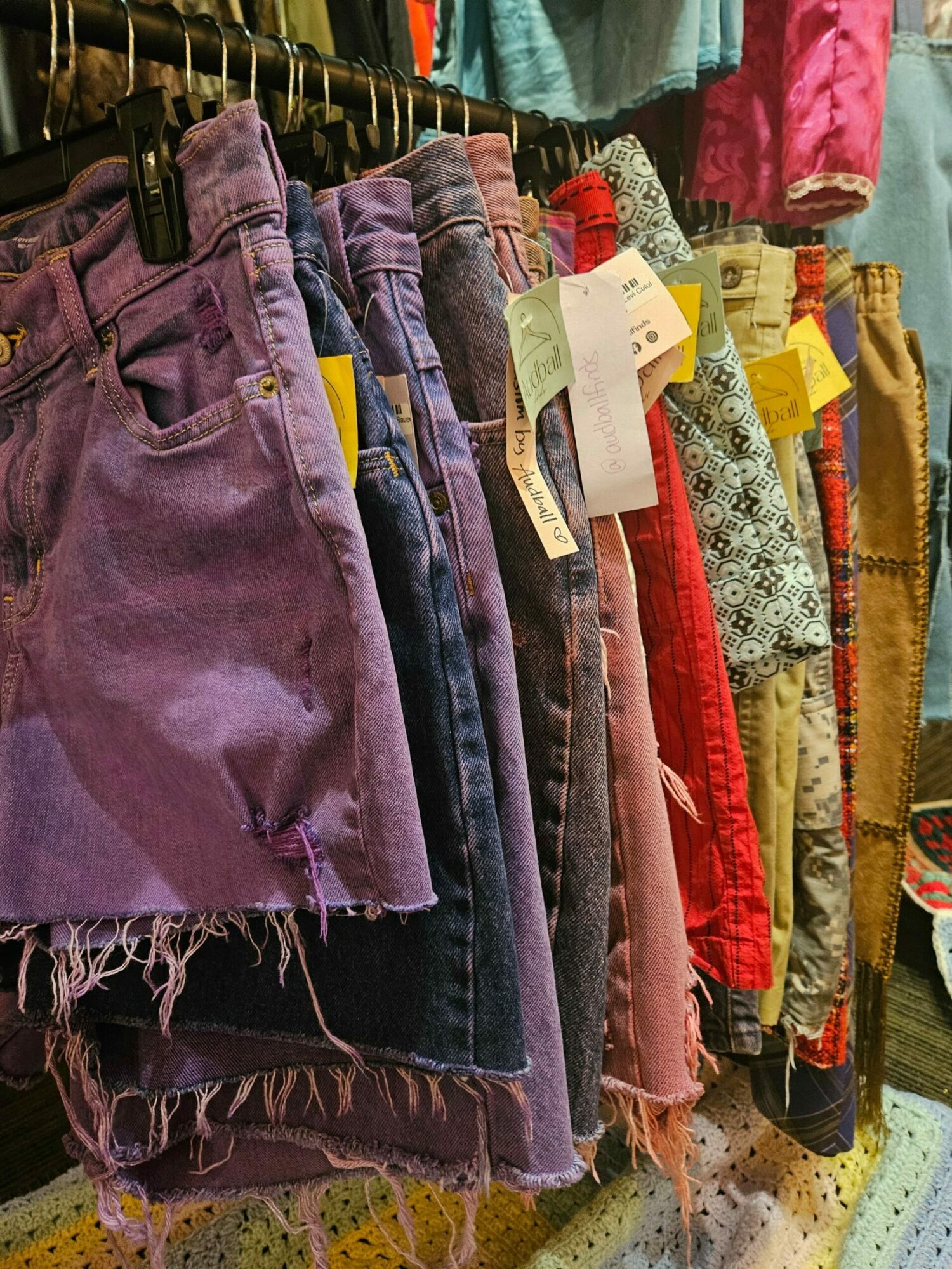 Stack of colorful fabric pieces with tags, some frayed edges, in a basket.