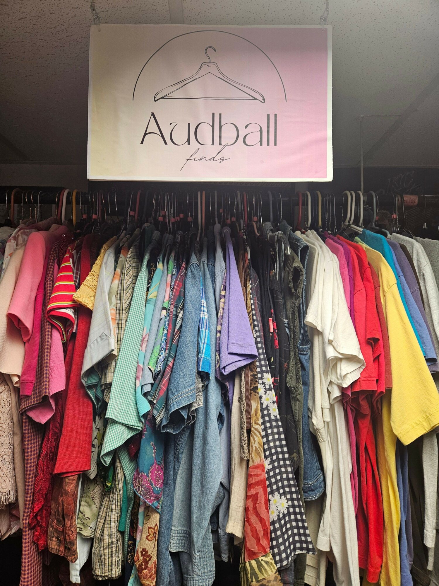Clothes stacked on a rack with a pink sign reading 'Aayball' and a logo, viewed sideways.
