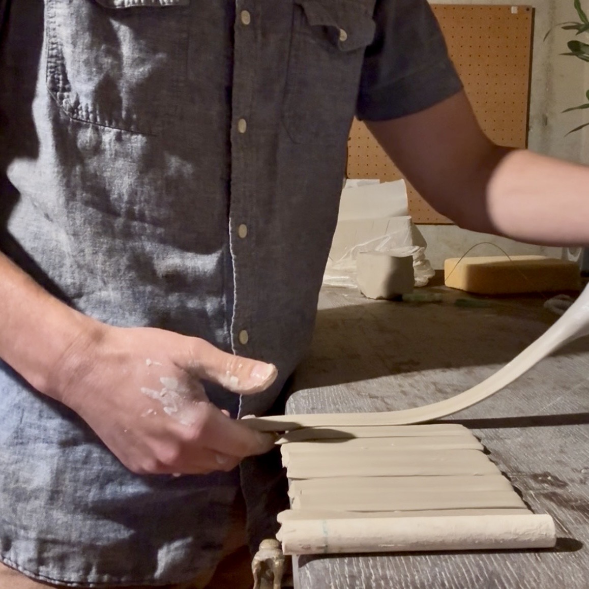 Person in a dark shirt rolling out dough on a wooden surface, with baking supplies in the background.