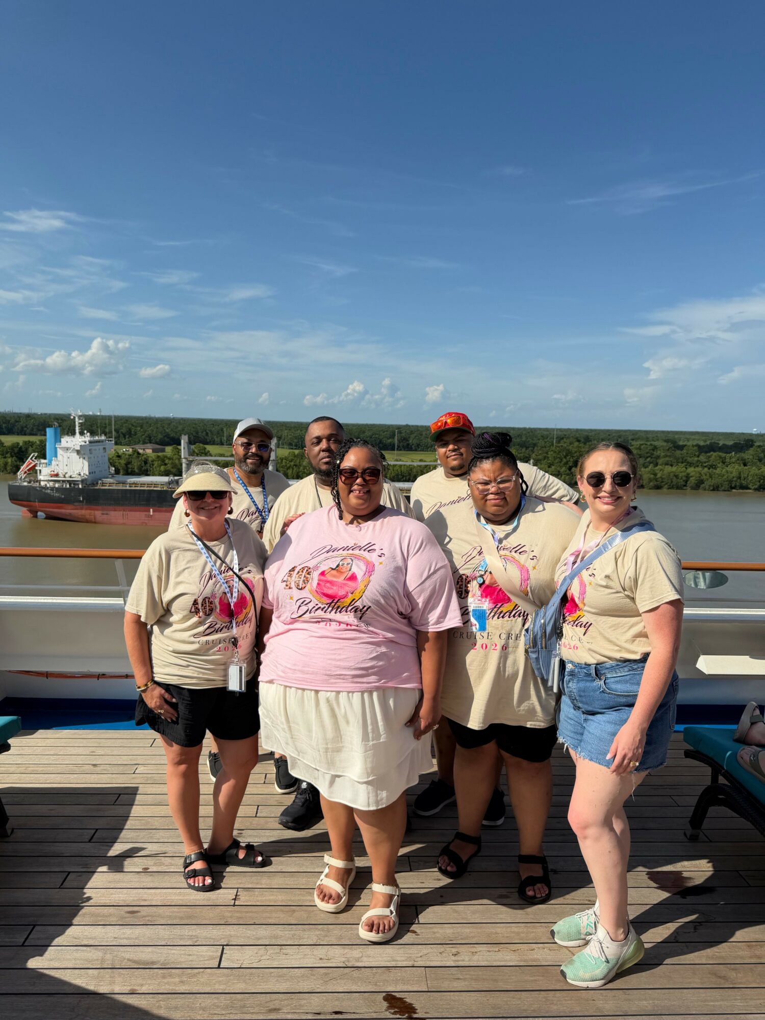 Group of people standing on a wooden dock near water, with a blue sky and clouds above.