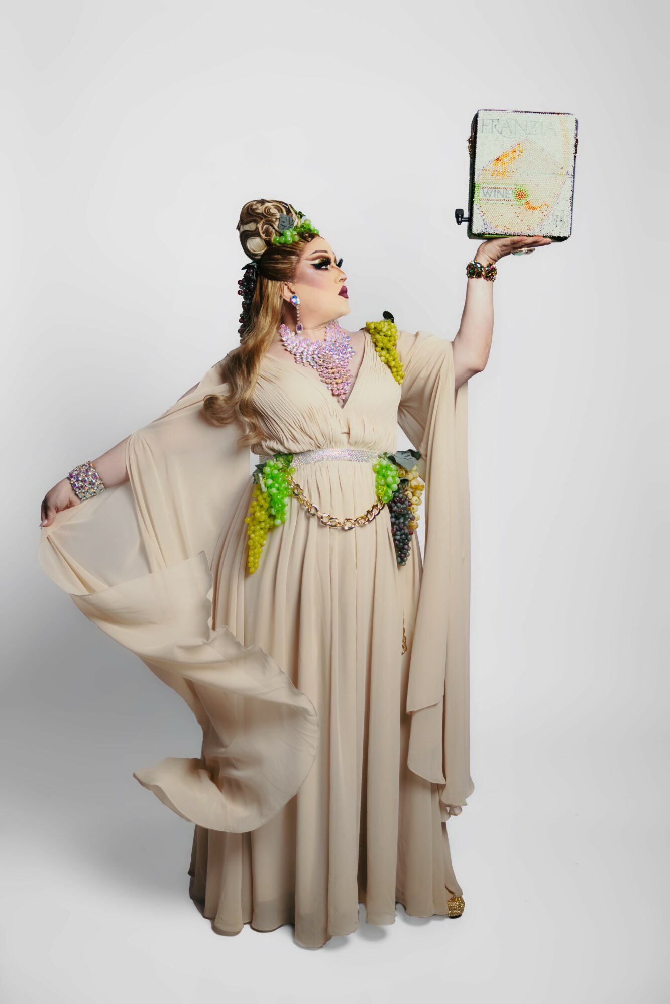 Person in elaborate costume holding a mirror, standing sideways, with a plain white background.