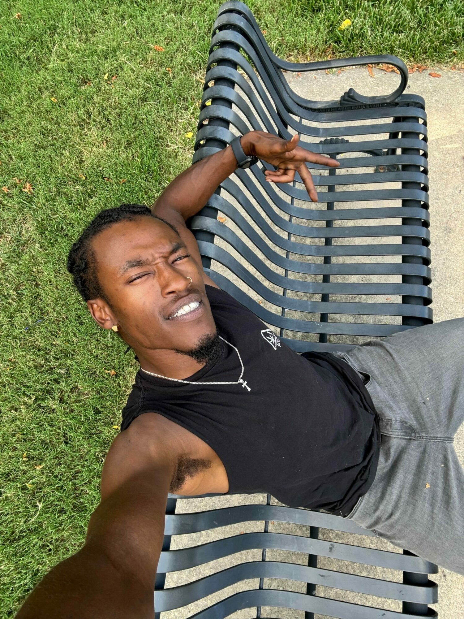 Person lying on a park bench, smiling, with grass and pavement in background.