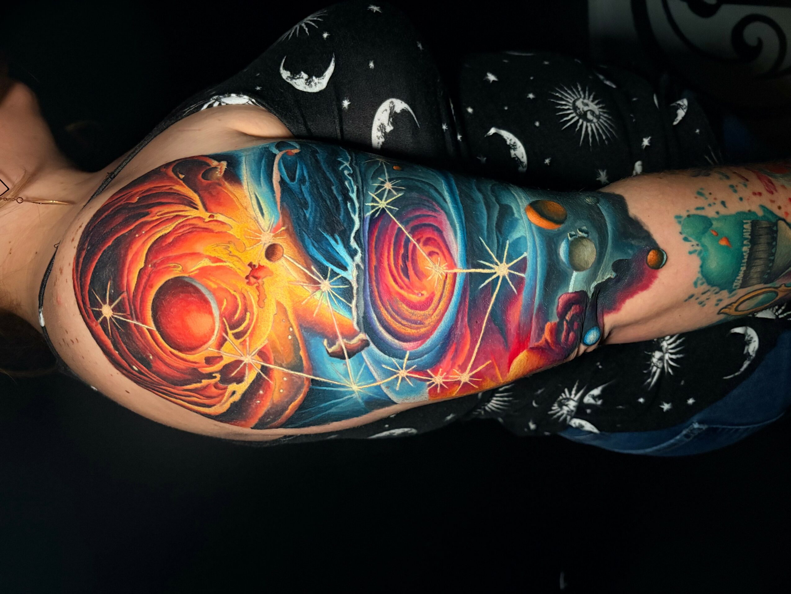 Colorful galaxy-themed tattoo sleeve with planets, stars, and cosmic elements on a person's arm.