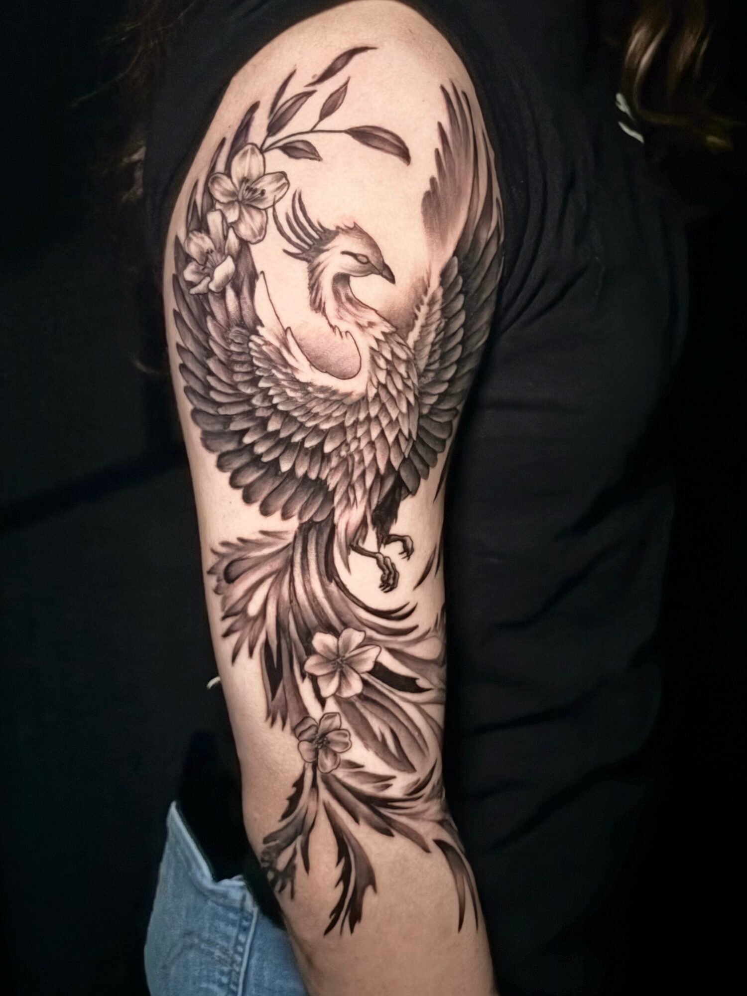 Black and gray tattoo of a swan with detailed feathers, surrounded by flowers and leaves on upper arm.