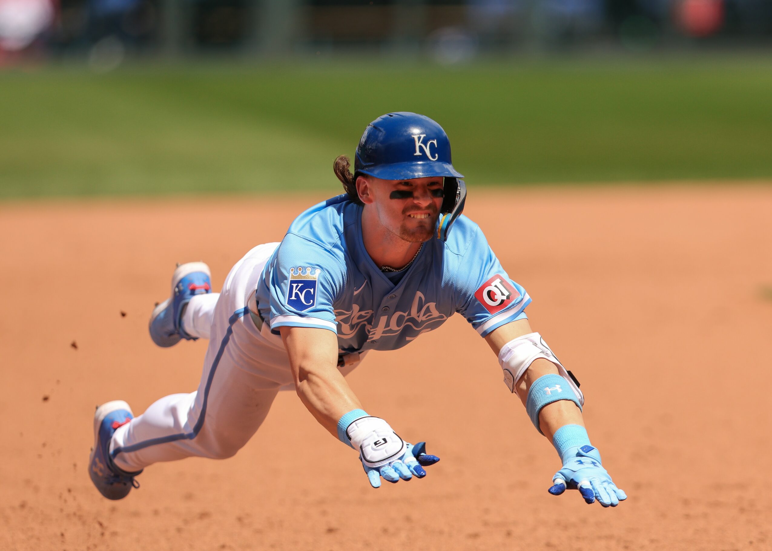 Baseball player diving on the field wearing a blue uniform and helmet, with a blurred background.
