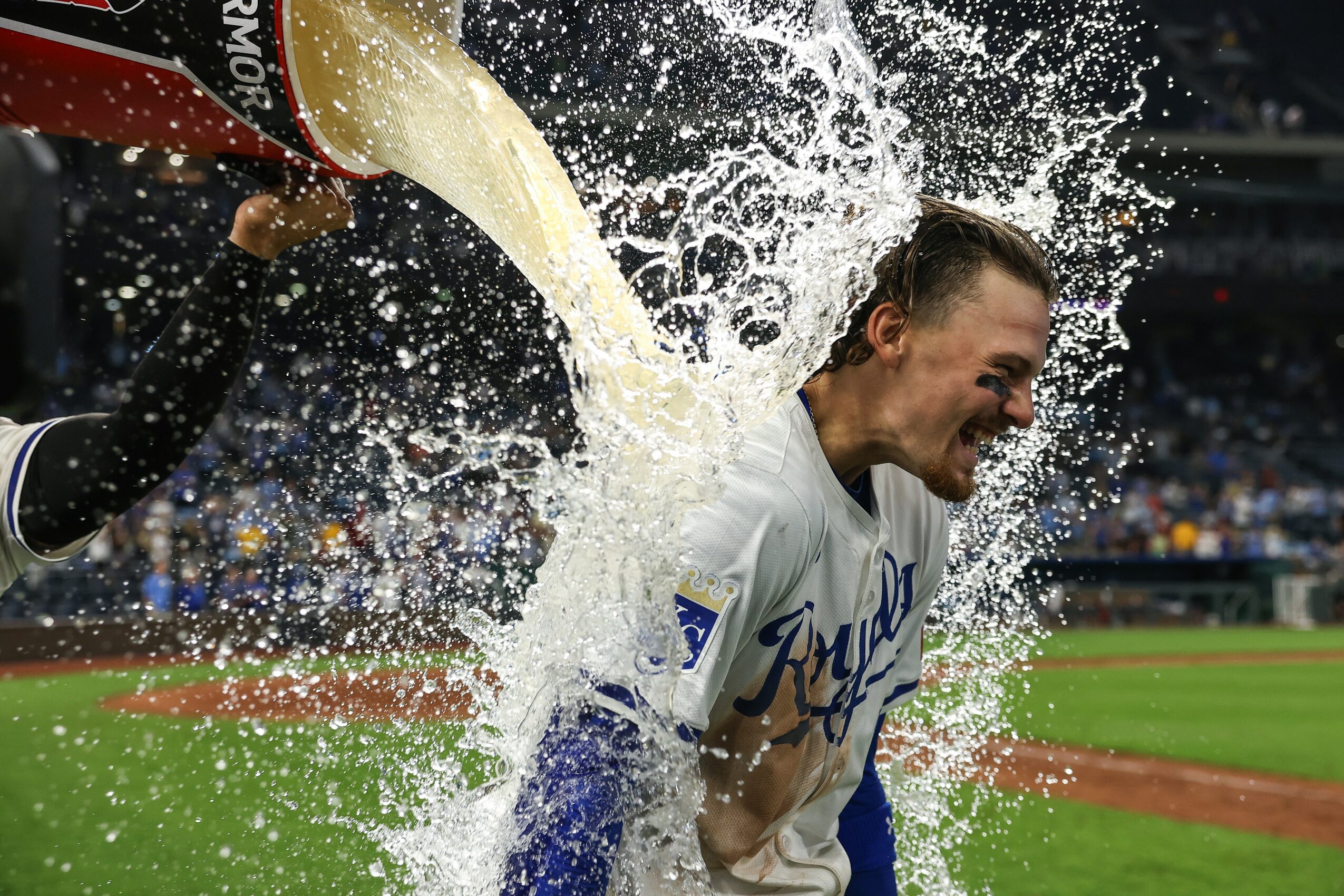 Person celebrating with water splash at a sports event, wearing a white jersey, in a stadium with a green field.
