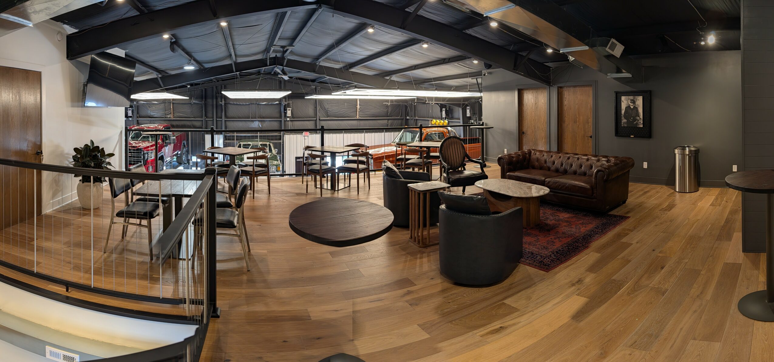 Modern lounge with seating, tables, and large windows, featuring wooden floors and a high ceiling with exposed beams.