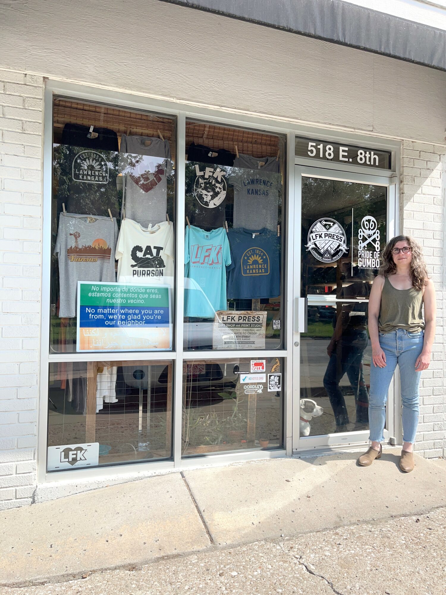 Person with sunglasses and long hair standing outside a store with sports merchandise display window.