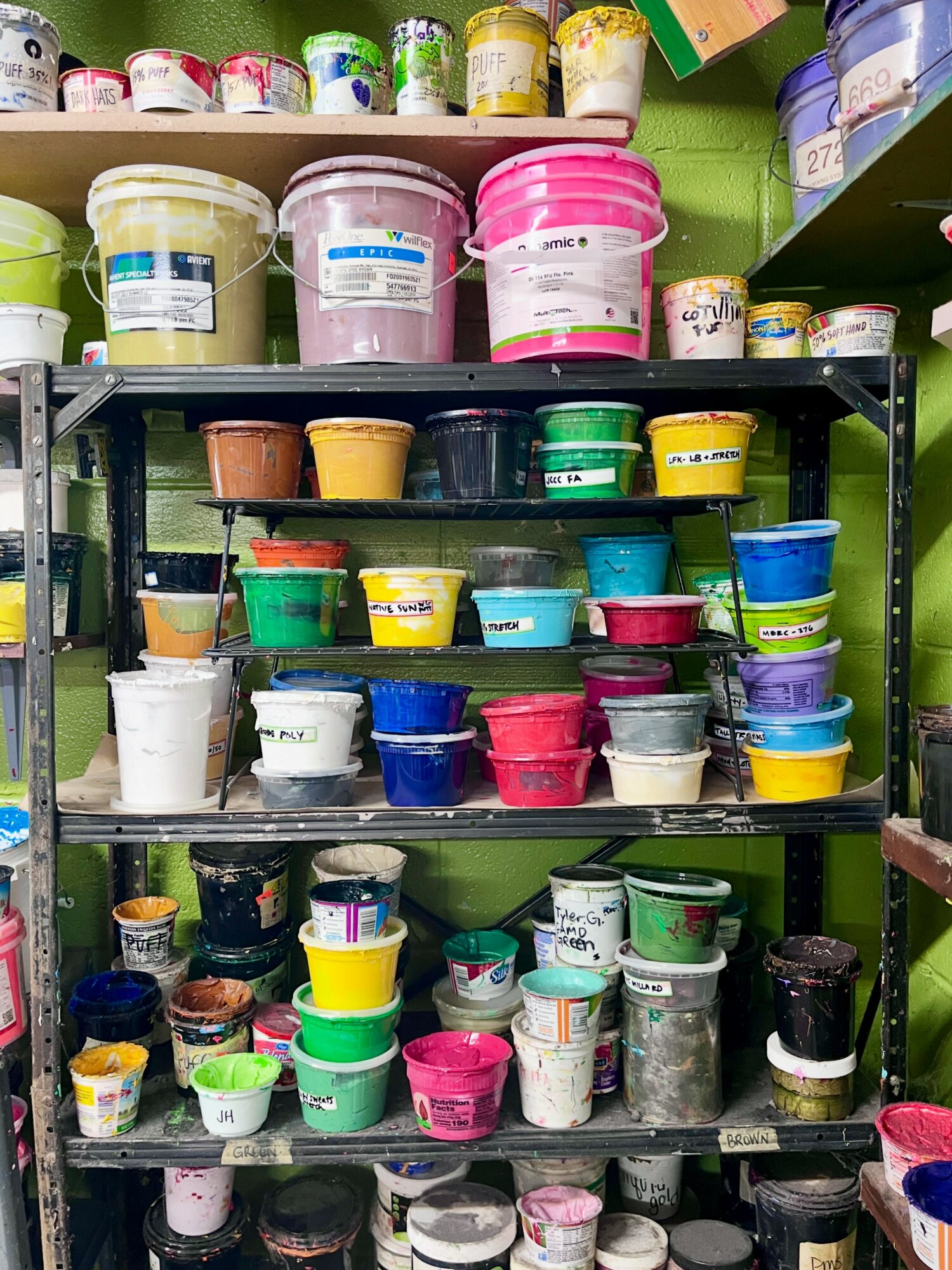Shelves filled with colorful buckets and containers of paint or similar products in a store.