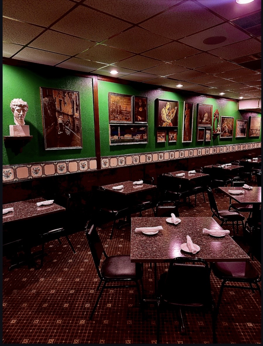 Dining area with tables set with napkins, against a green wall decorated with framed artwork and sculptures.