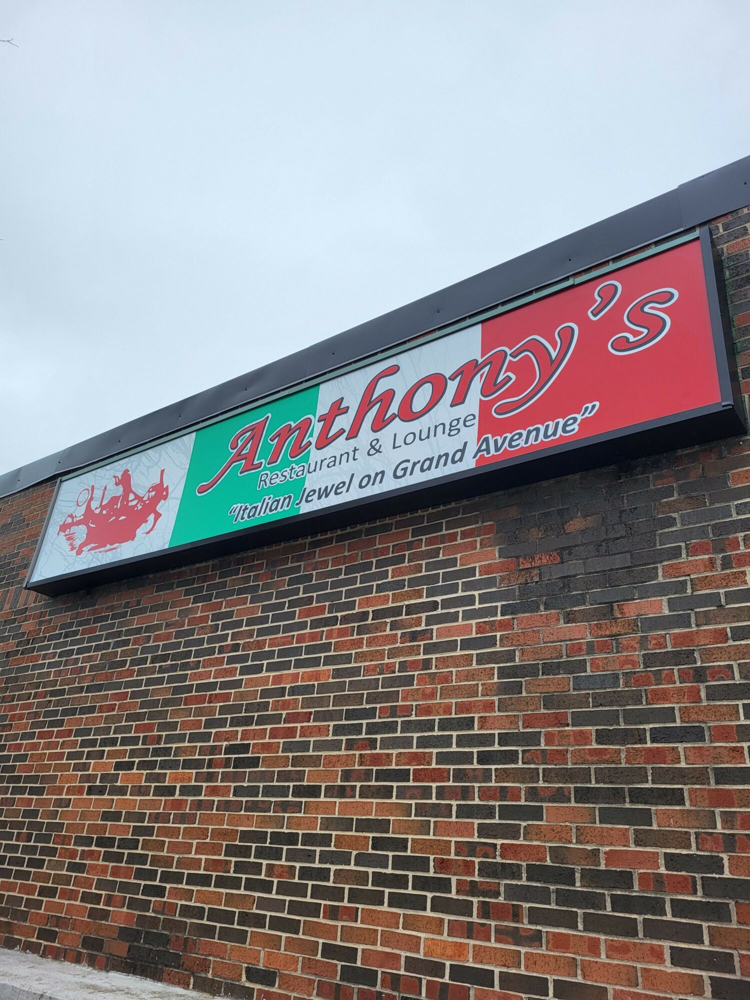 Signboard with red, white, and teal colors on a brick wall, displaying text and a lion logo.