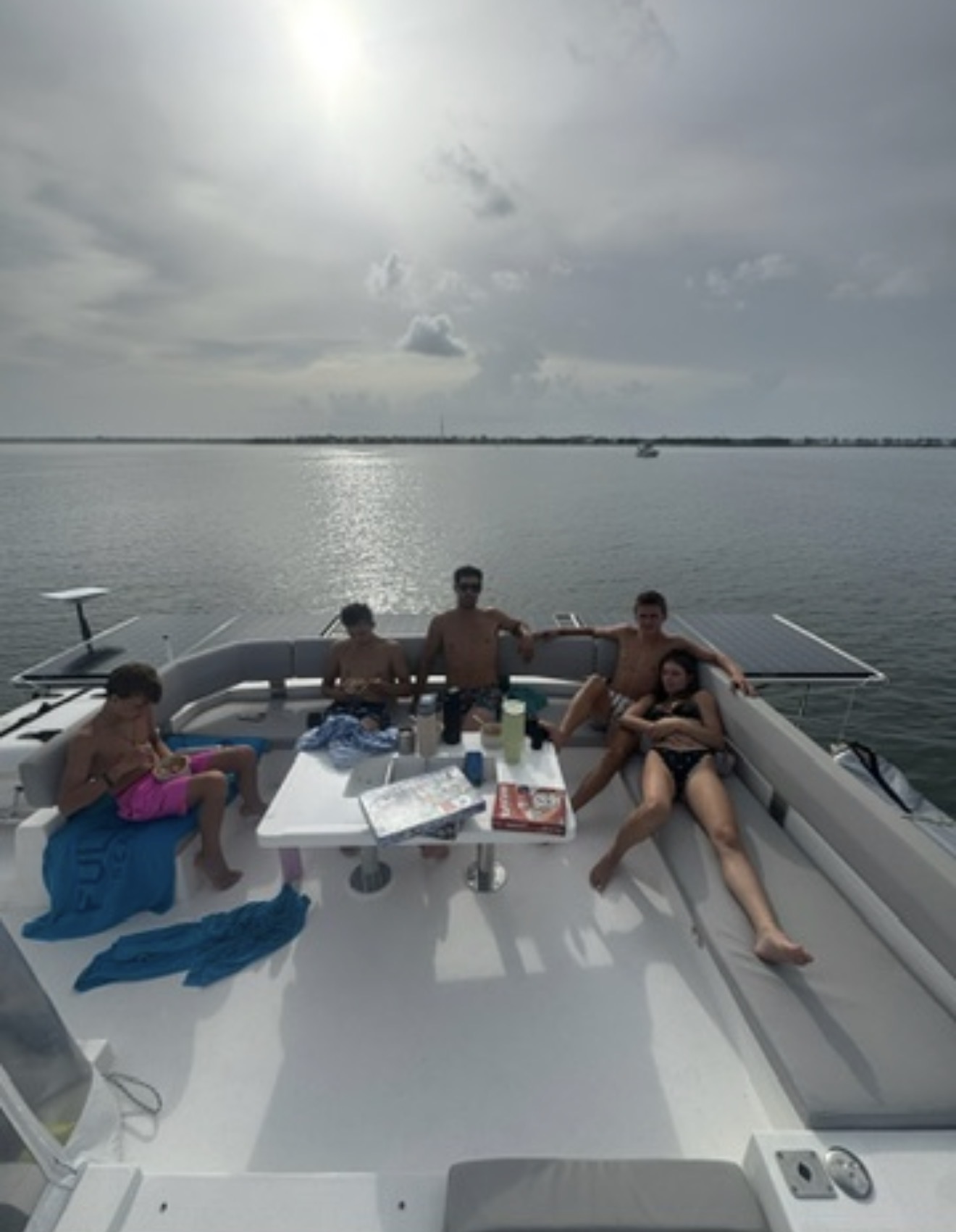 Four people relaxing on a boat with a calm water body and cloudy sky in the background.