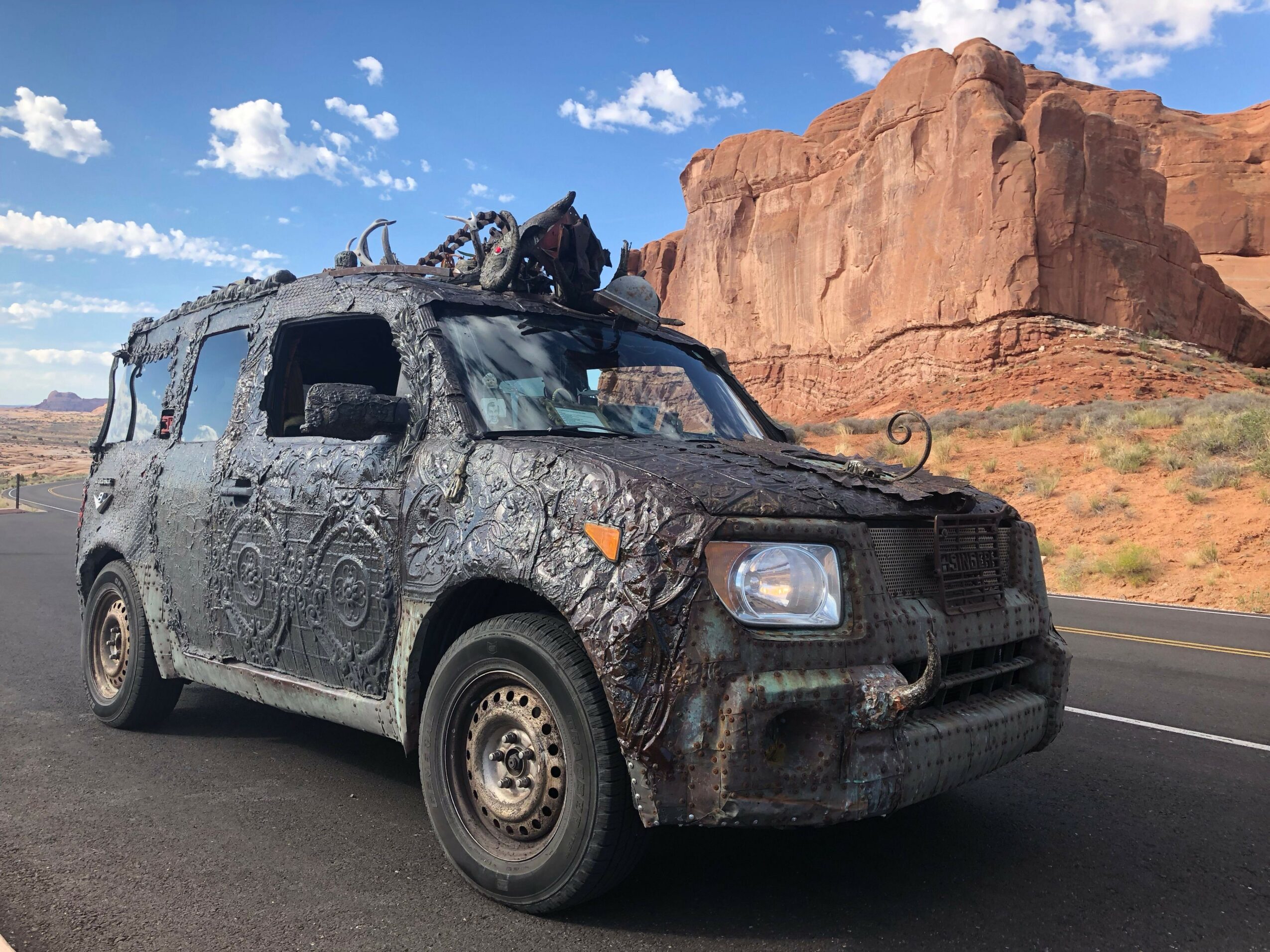 Upside-down image of a damaged car on a road with a rocky landscape and blue sky.