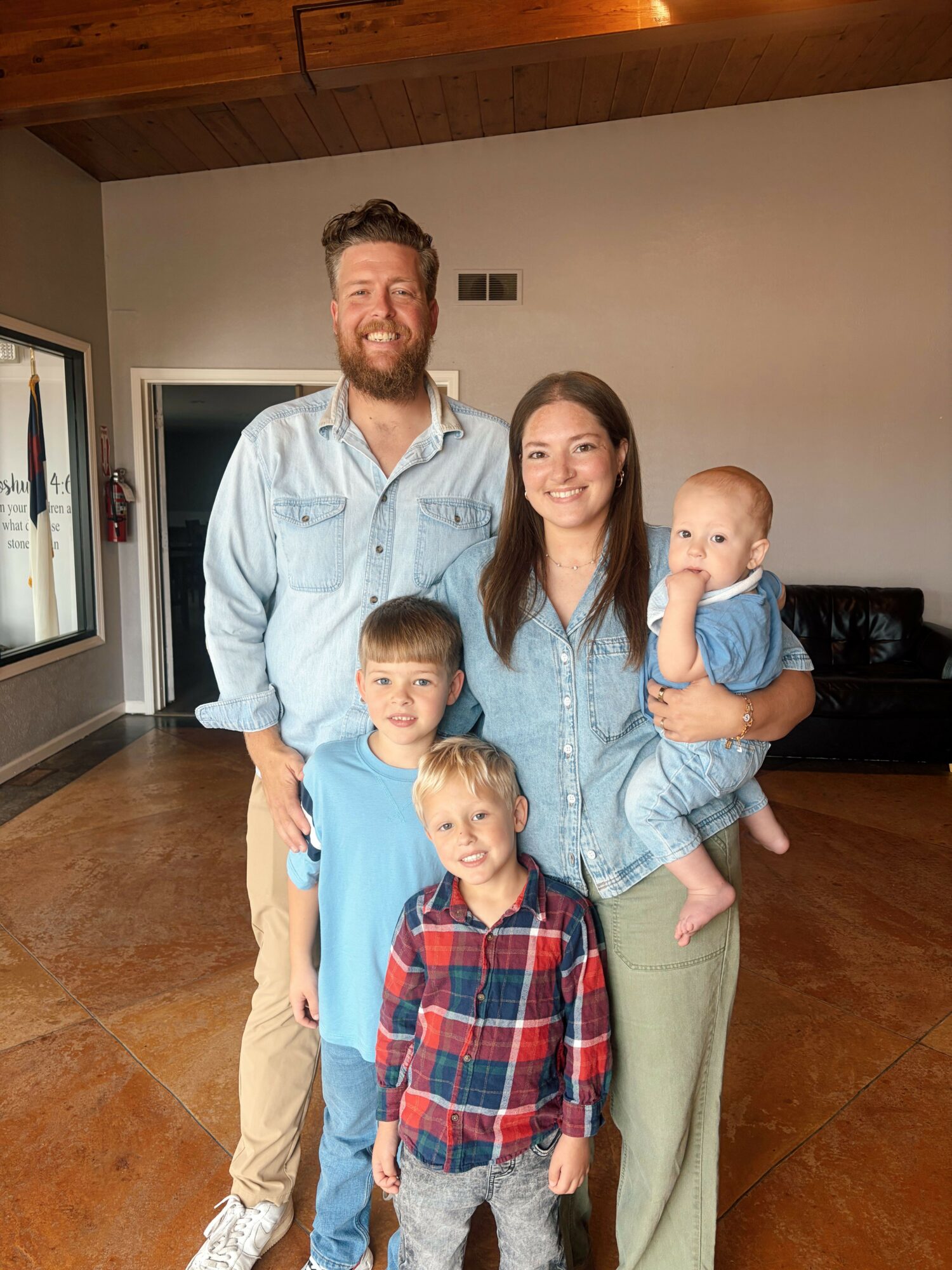 Four people, two adults and two children, standing together indoors, smiling at the camera.