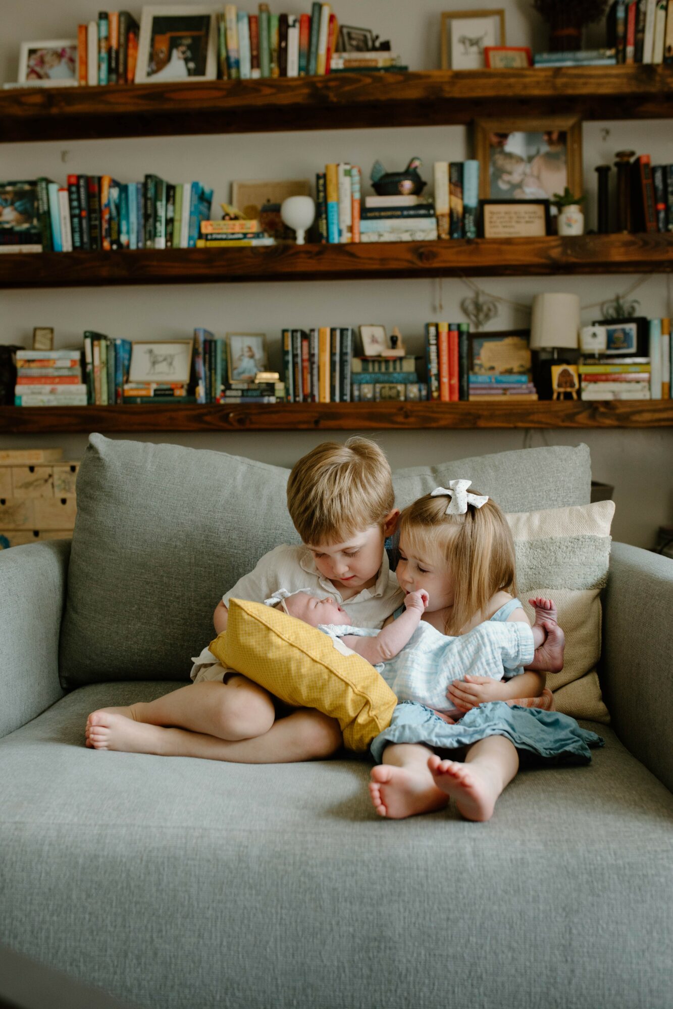 Two children sitting on a sofa, looking at a yellow object, with a bookshelf in the background.