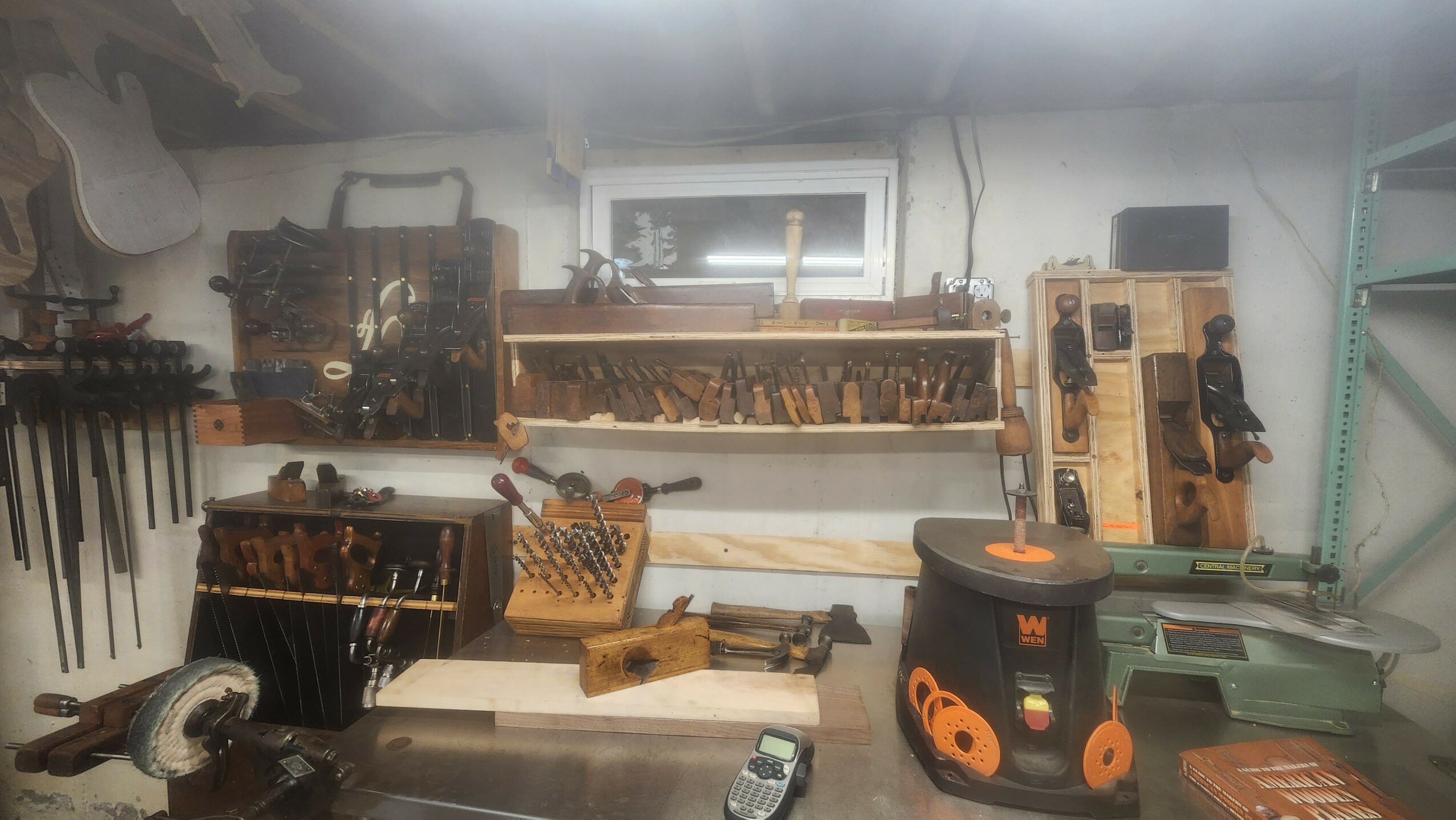 Workshop with tools and equipment on shelves and workbench, small window above, organized workspace.