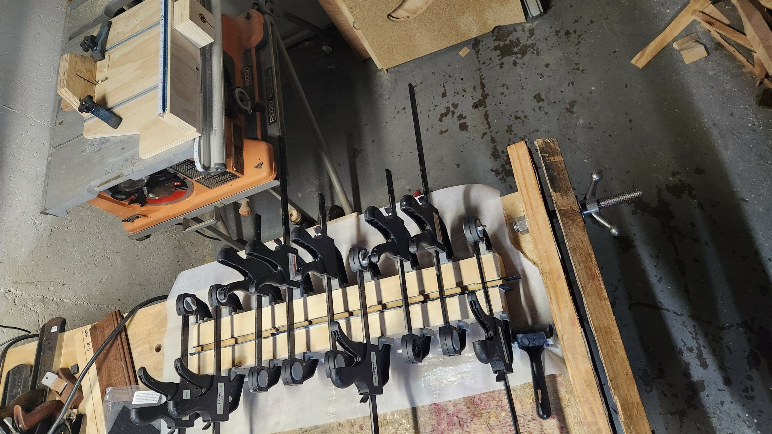 Woodworking clamps attached to a wooden board on a workbench in a workshop.
