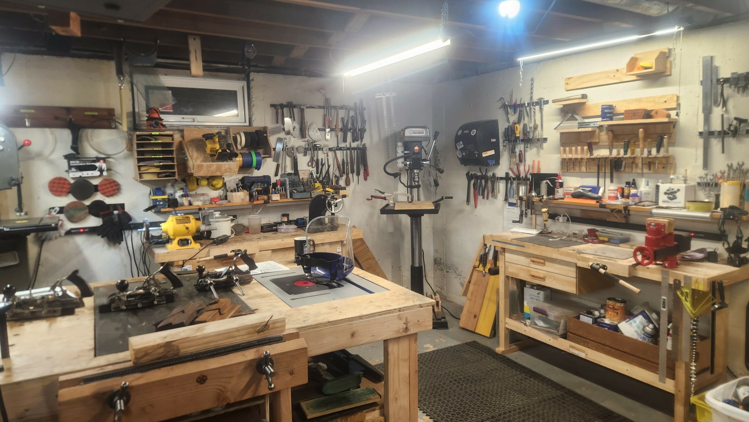 Workshop with workbenches, tools, and equipment organized on walls and shelves, illuminated by bright overhead lights.