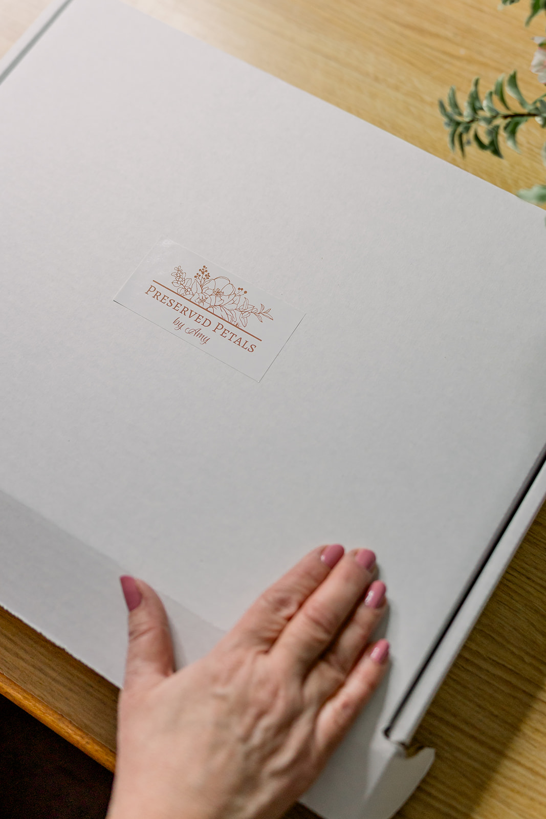 Hand resting on an open book with a logo and text on the page, on a wooden surface.