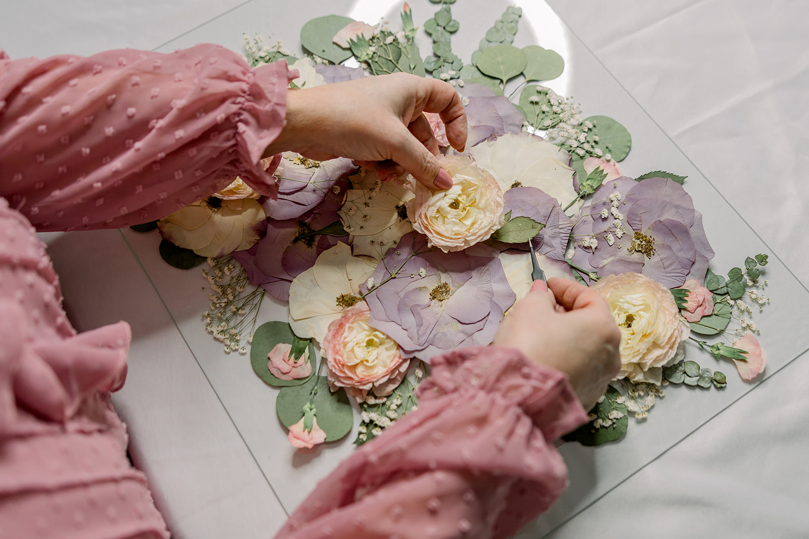 Person arranging paper flowers on a decorative surface with floral patterns, wearing pink long sleeves.