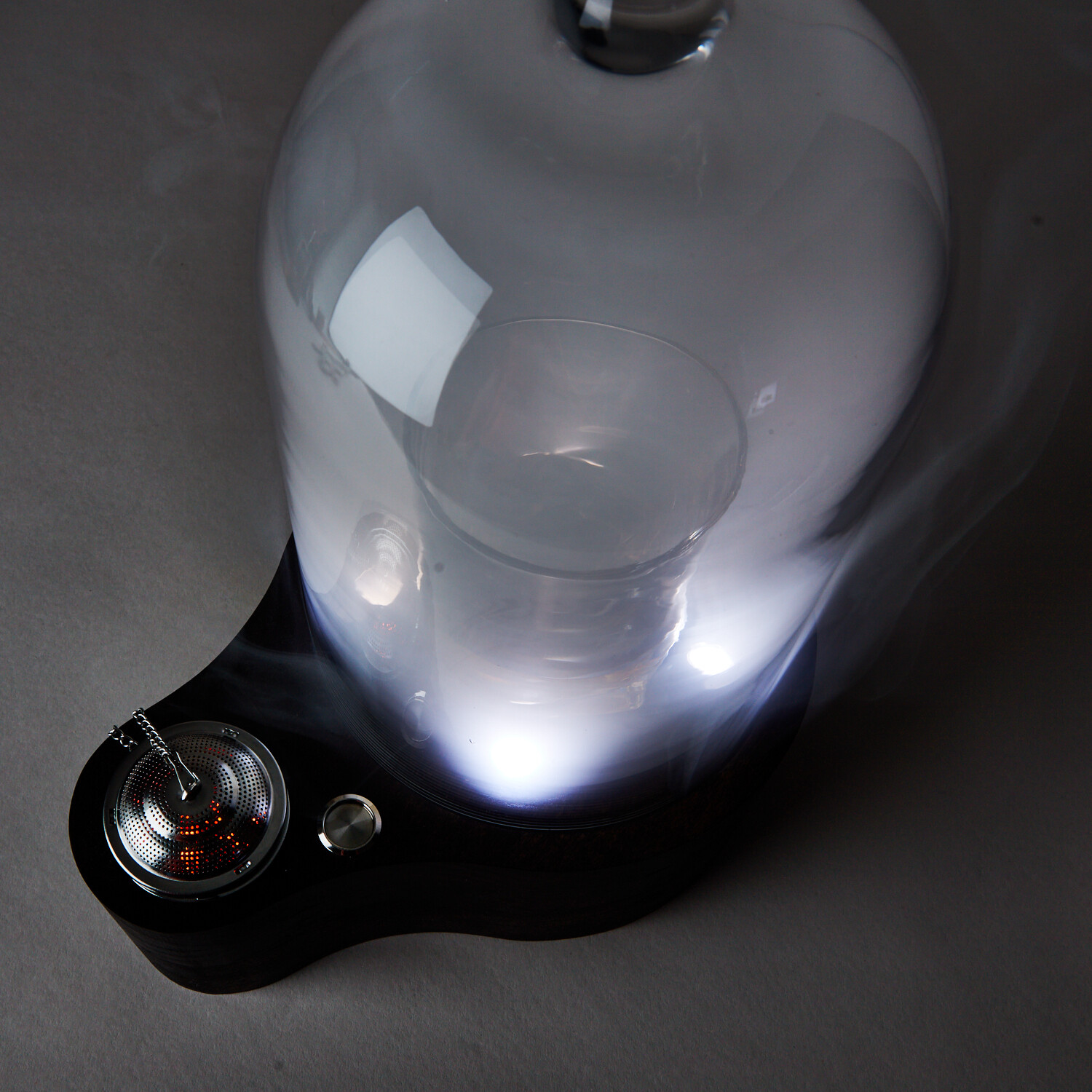Close-up of a transparent container with a black base and a small metallic component, illuminated from below.
