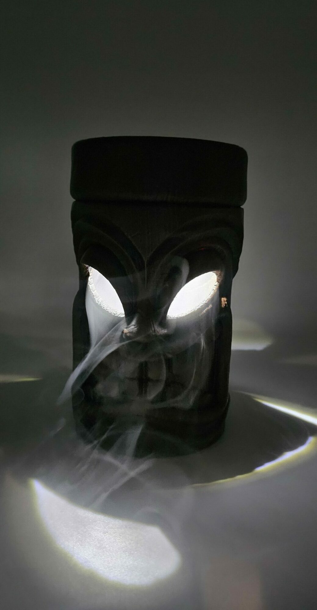 Black camera with lens facing upward, emitting smoke or vapor, on a dark surface with light reflections.