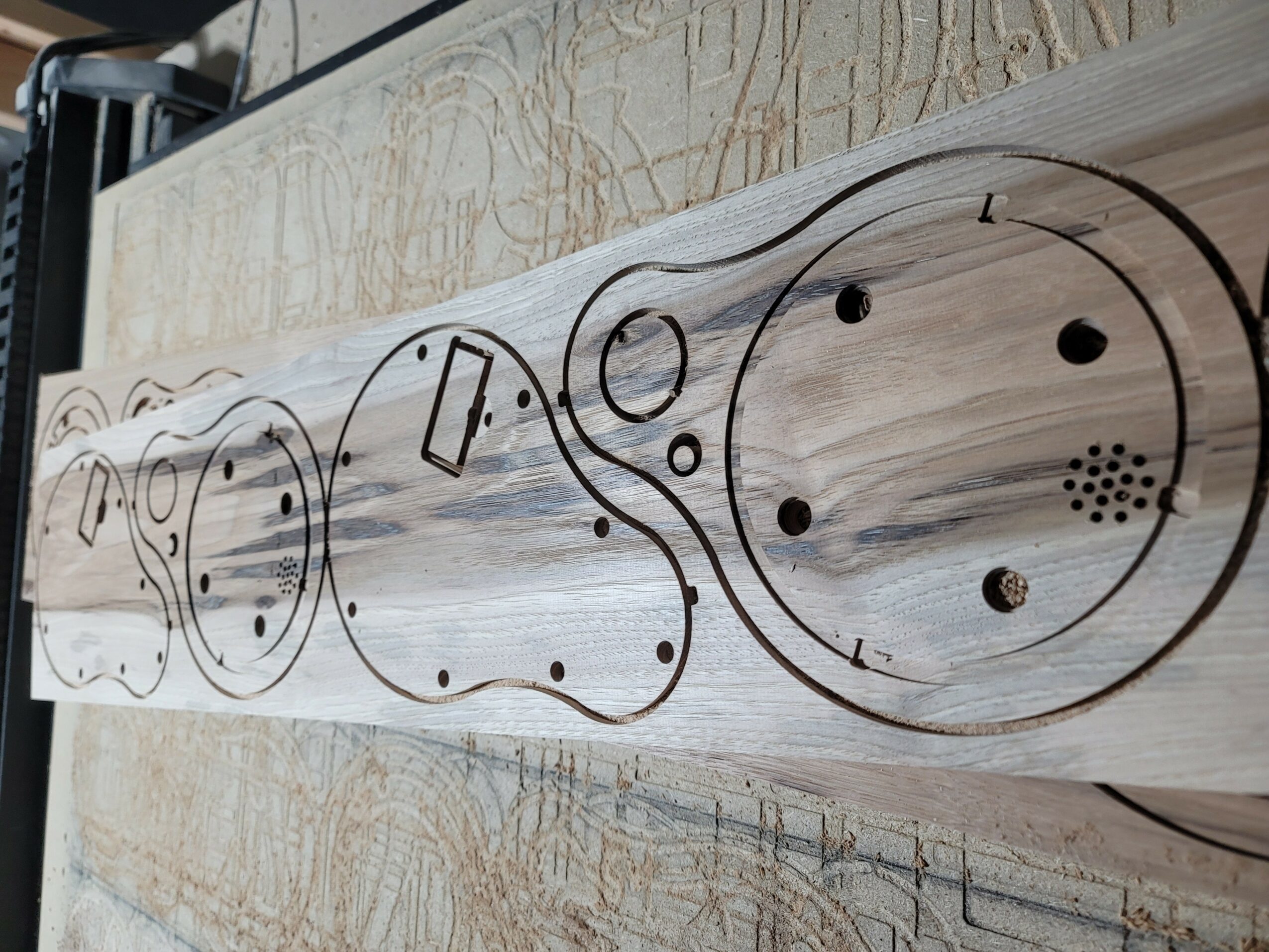 Long wooden board with circular and irregular shapes drawn on it, placed on a textured surface.