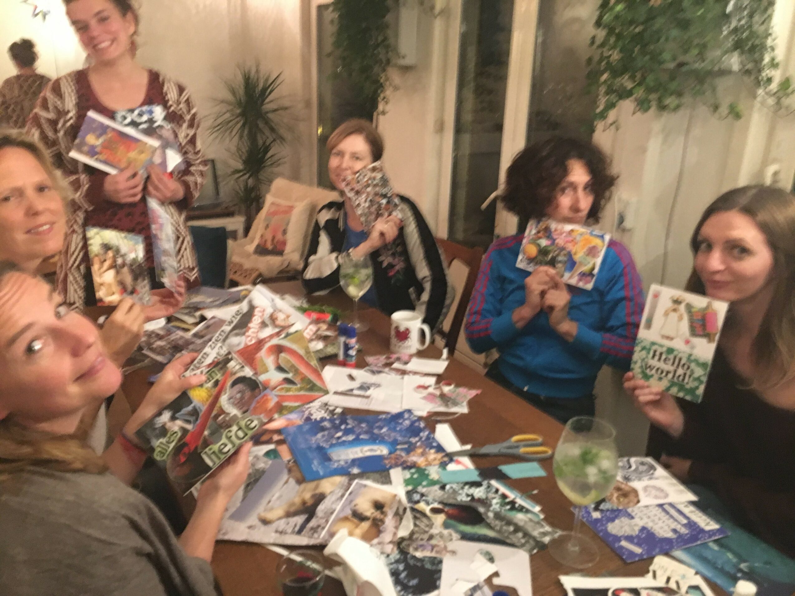 Group of women sitting around a table with magazines, scissors, and craft supplies, smiling and engaging in a craft activity.
