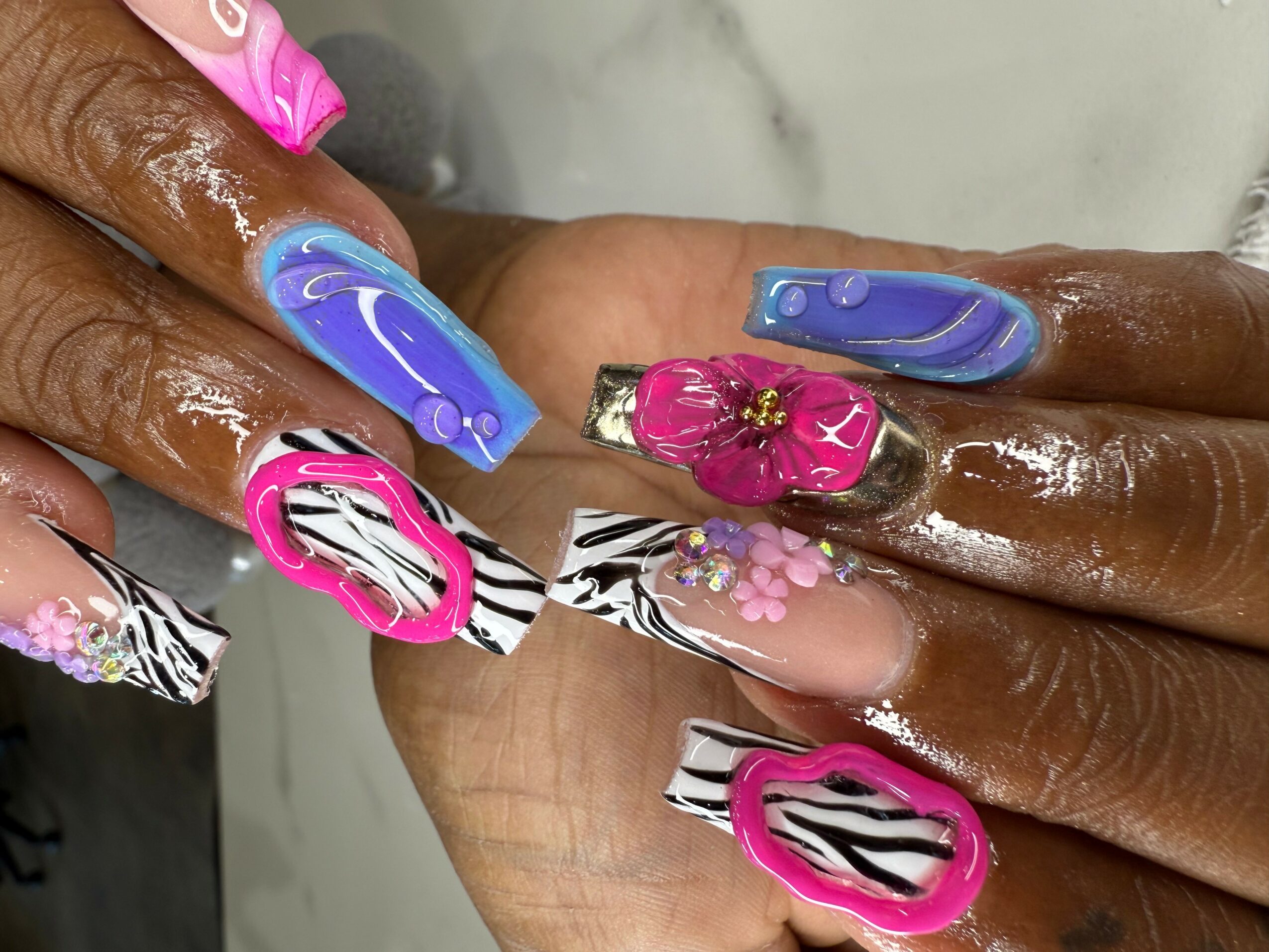 Close-up of hands with colorful, decorated nail art, including pink, blue, and zebra patterns, with some nails having floral designs.