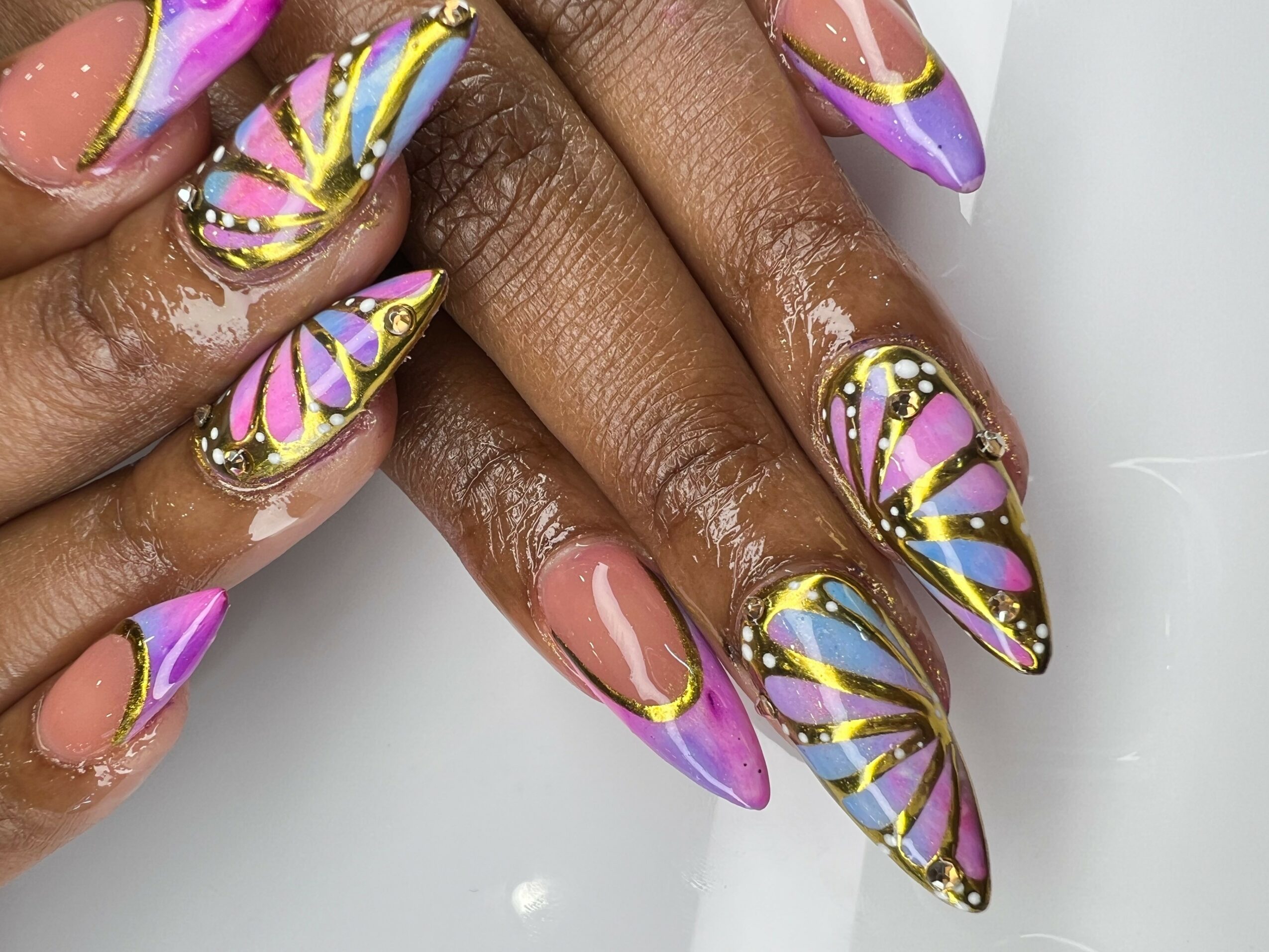 Close-up of hands with colorful, decorated nails featuring purple, pink, yellow, and blue designs with gold accents.