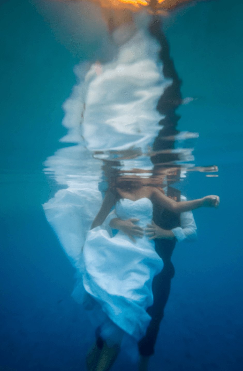 Person in a white dress underwater, with their reflection visible on the water surface.