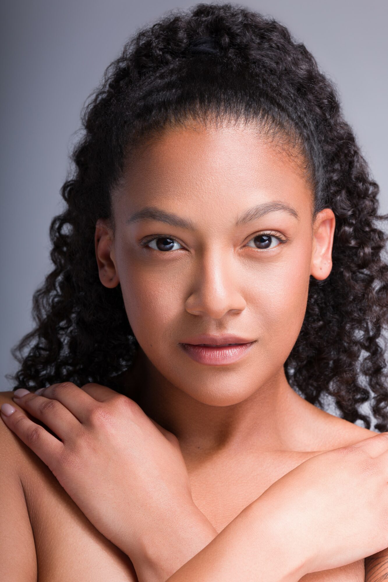 Portrait of a young woman with curly hair, looking directly at the camera with crossed arms.