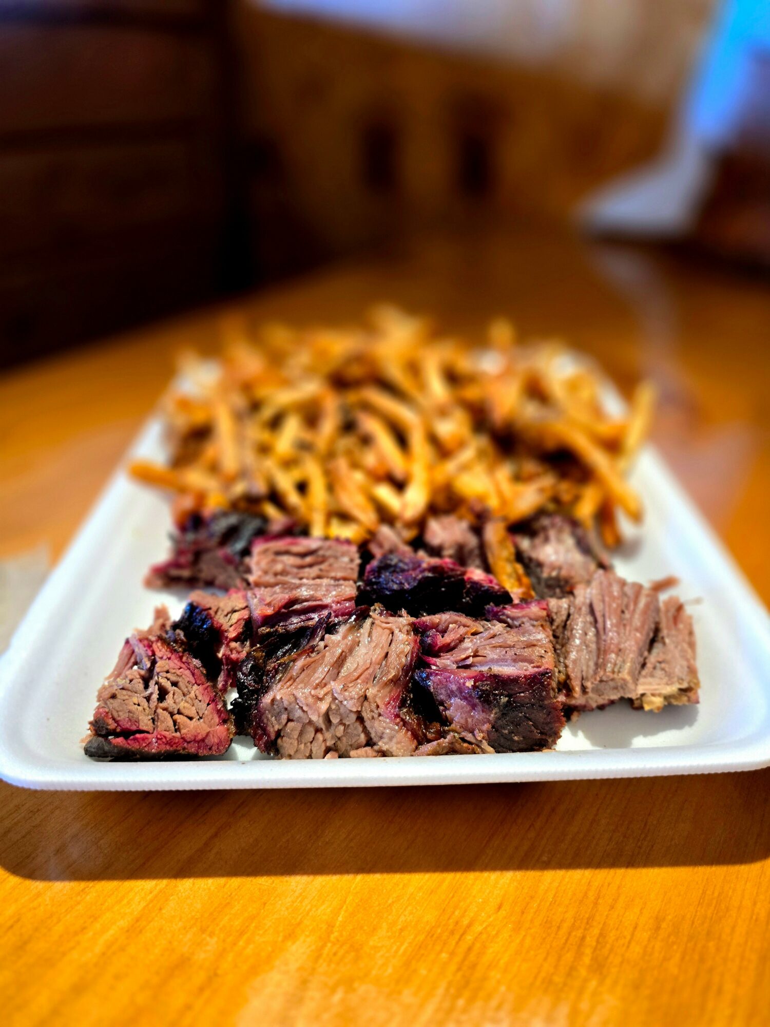 Cooked beef slices and pasta on a white rectangular plate, placed on a wooden table.