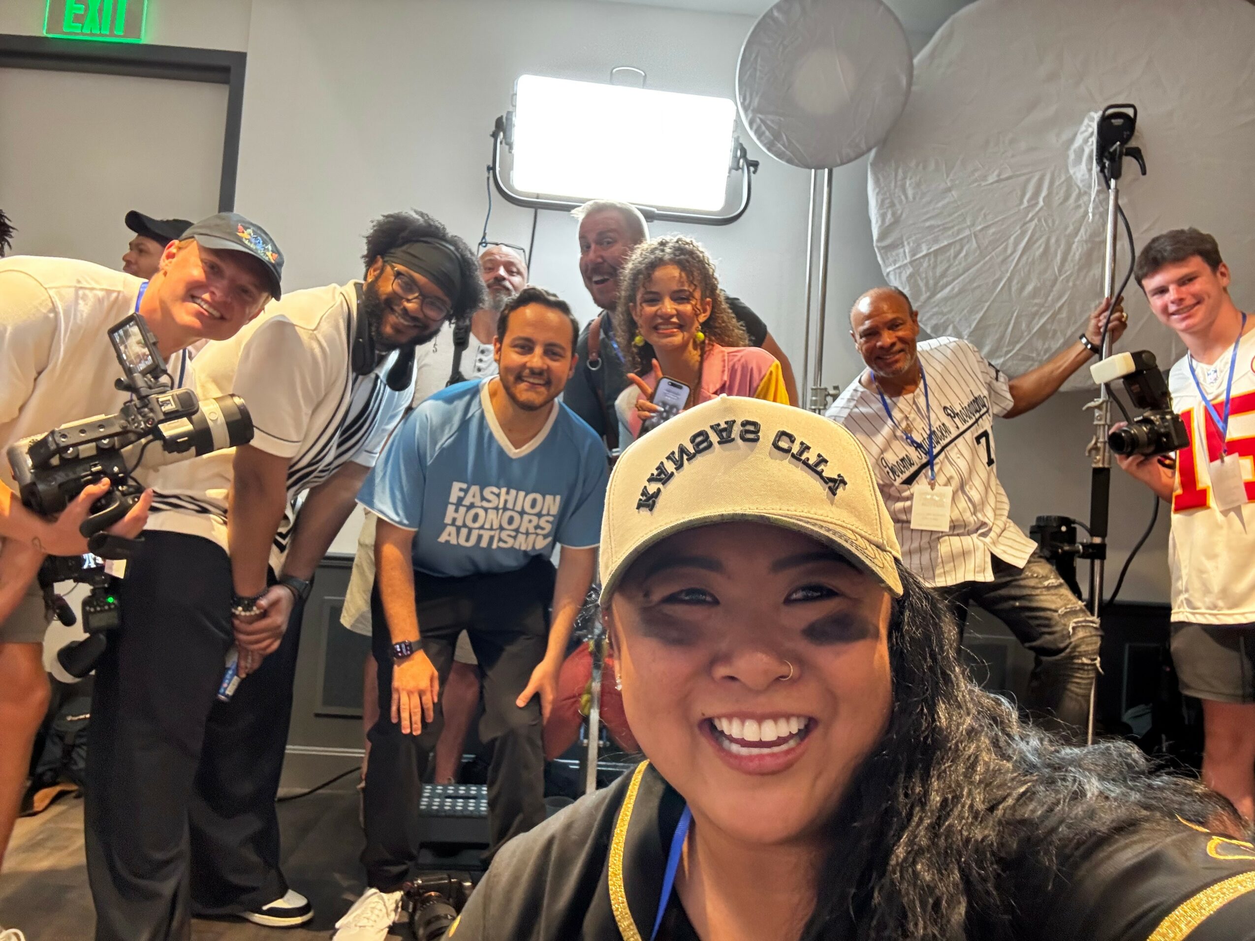 Group of people smiling and posing for a photo in a studio setting, with a woman in the foreground wearing a cap.
