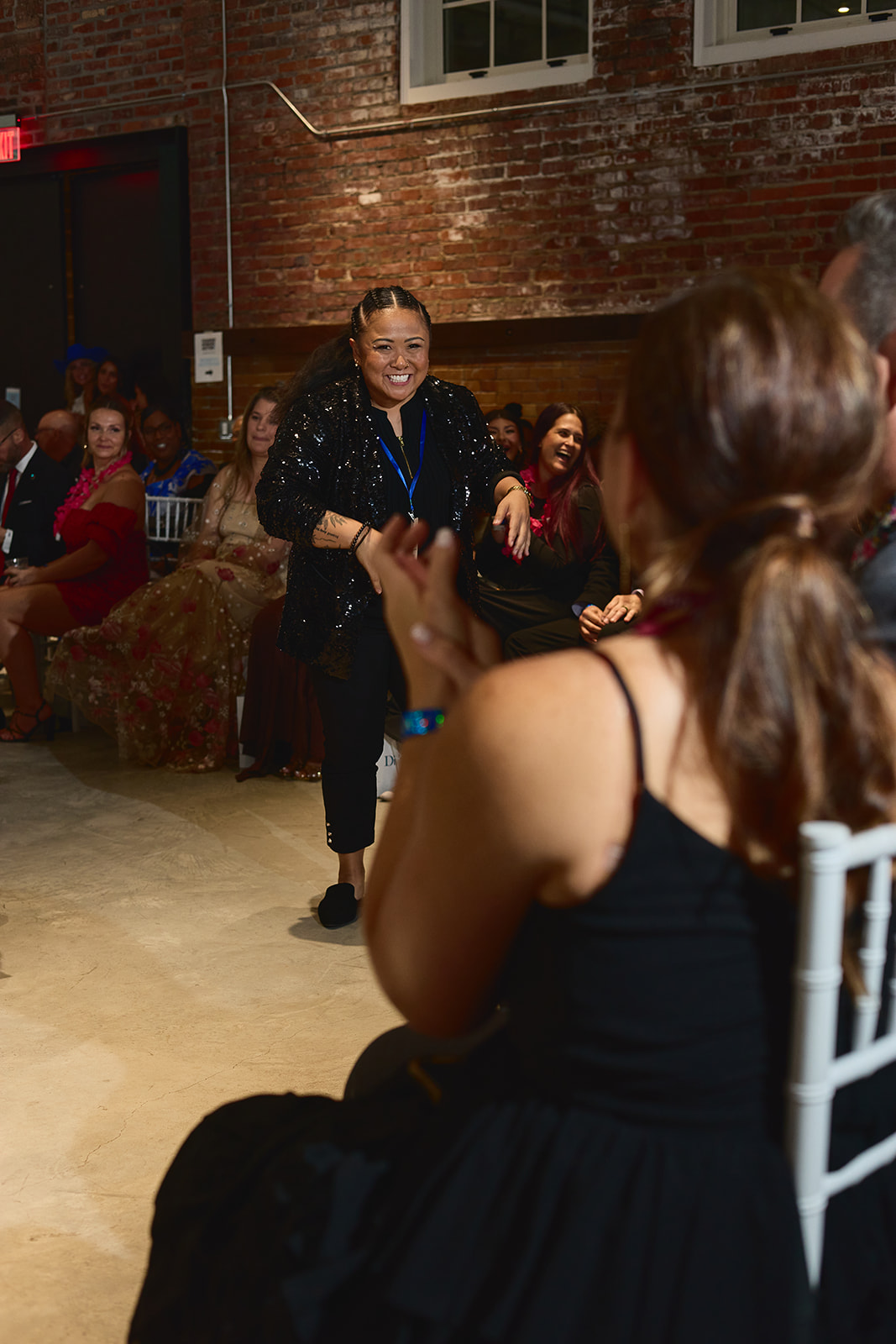 Woman dancing and smiling at a social event with people seated in the background.