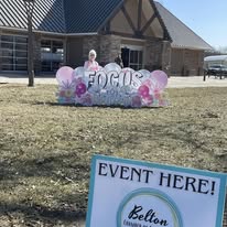 Decorative sign with balloons and flowers in front of a building, indicating an event at Belton.