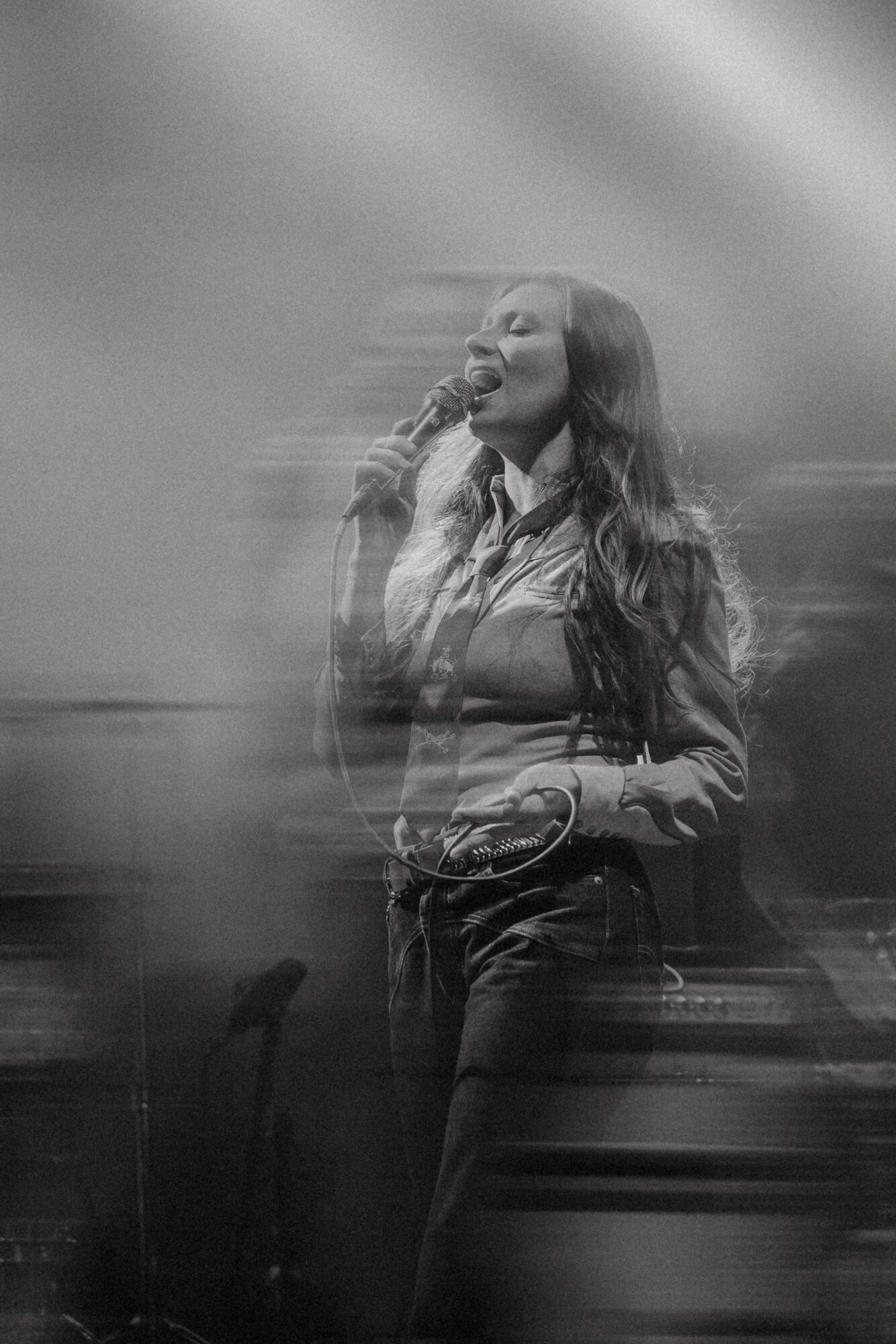 Woman singing into a microphone on stage with motion blur, in black and white.