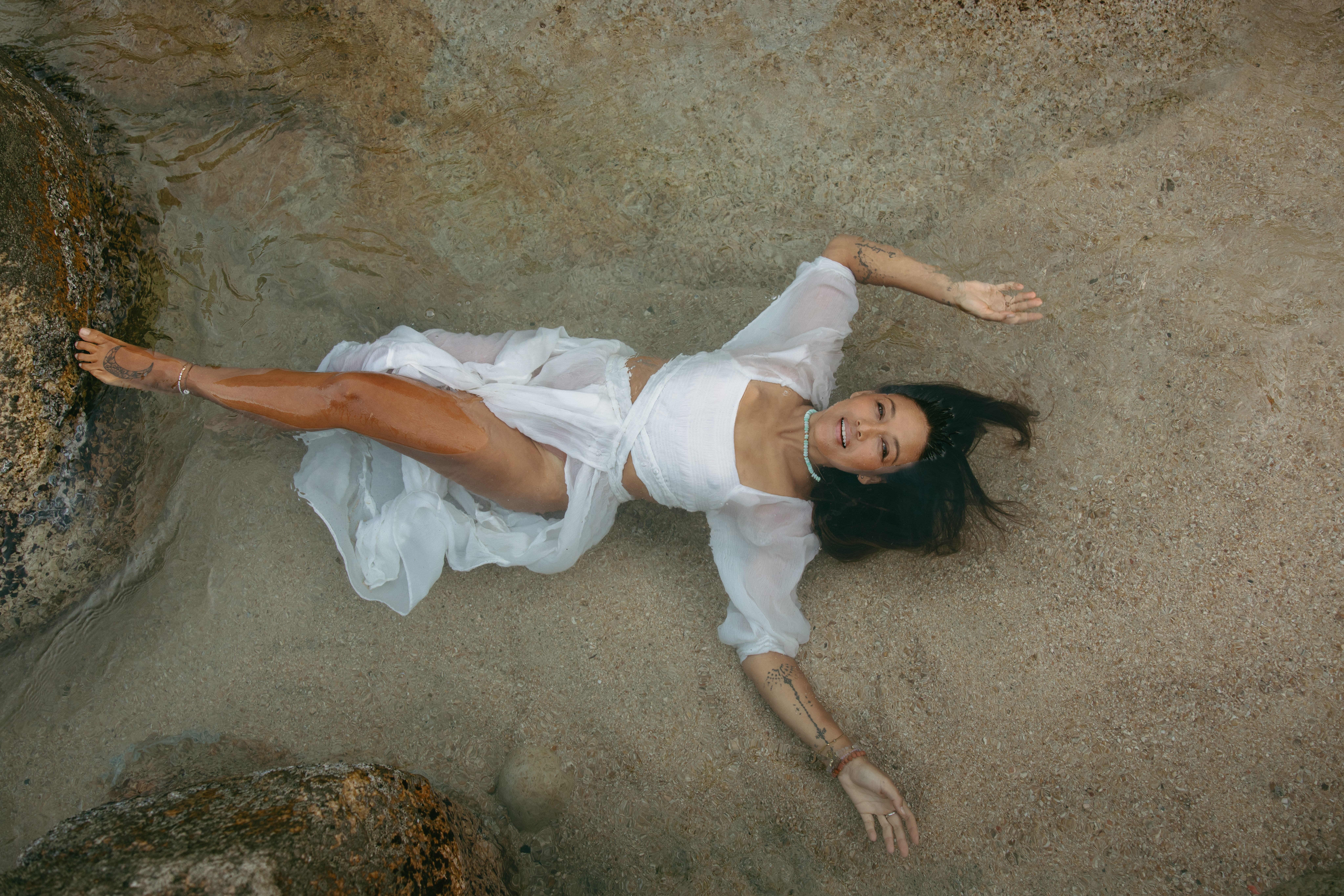 Woman lying on ground in white dress, arms and legs extended, looking at camera.