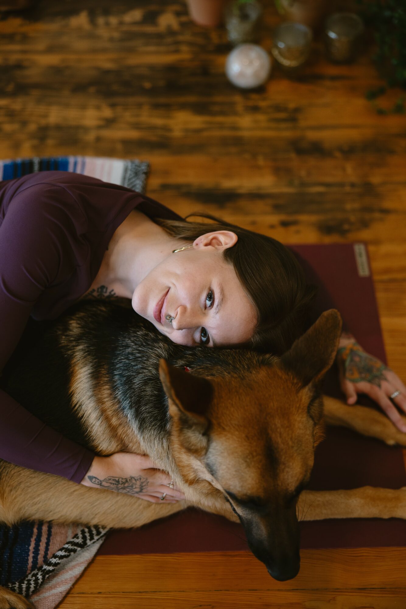 Woman lying on the floor with a dog, both resting their heads together on a wooden floor.