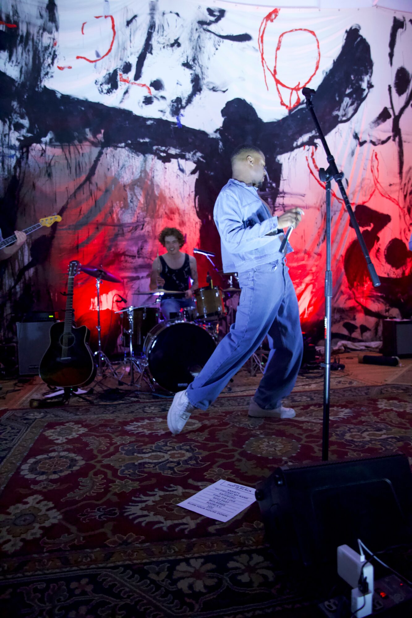 Person singing into a microphone on stage with a band, colorful abstract background, and musical instruments, performing live.
