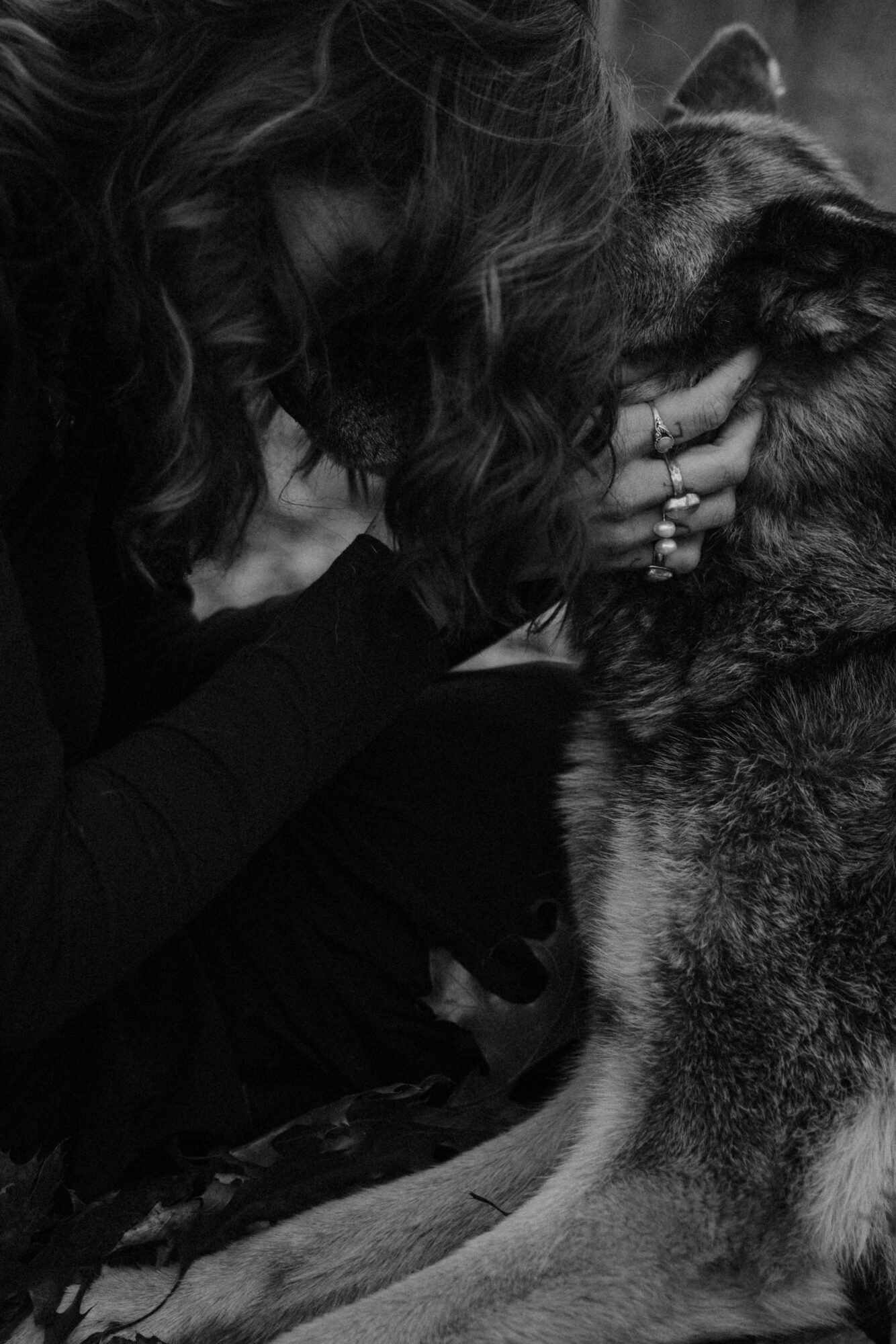 Person with curly hair gently touching a dog’s face, both facing each other closely, in black and white.