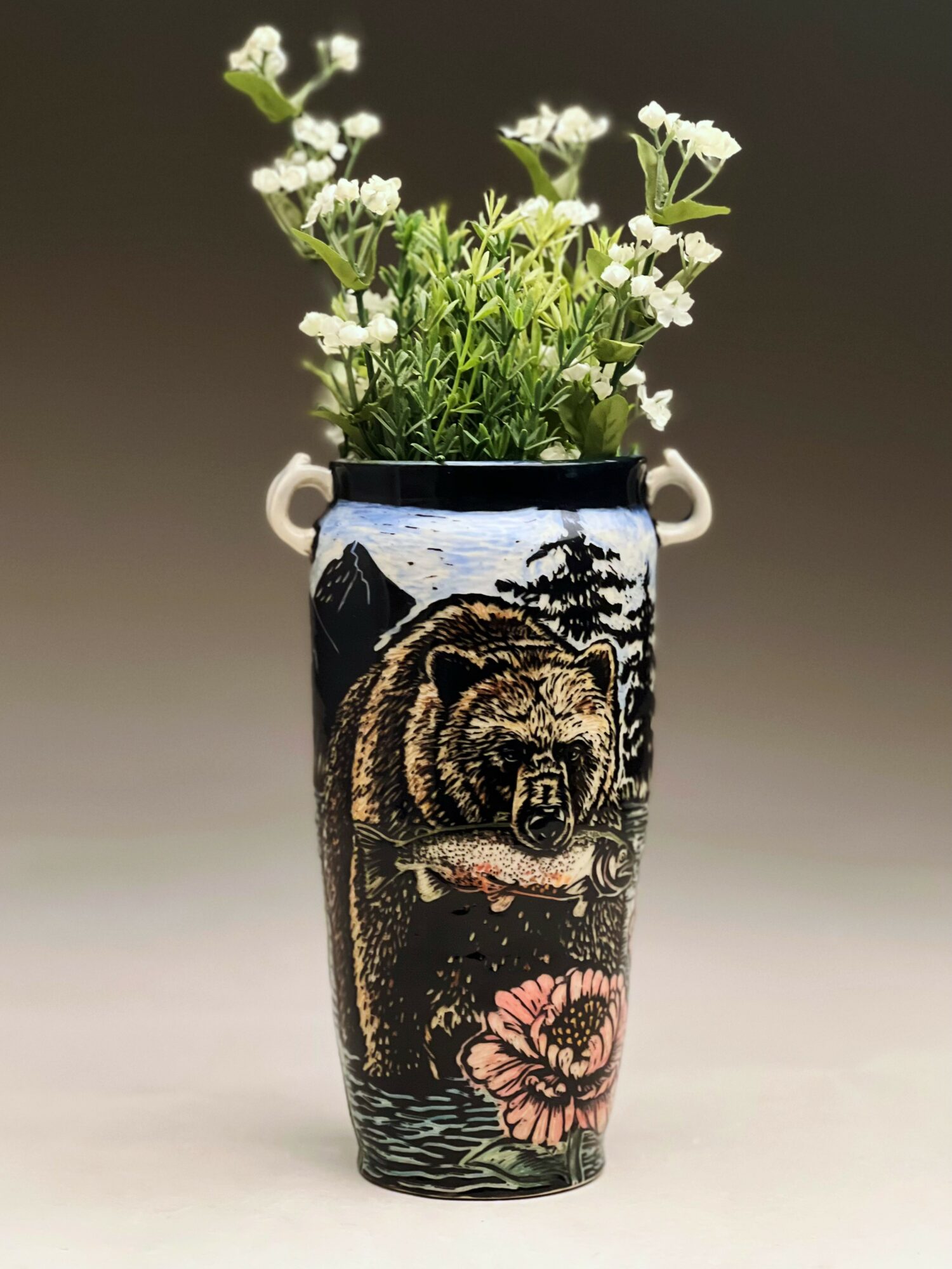 Vase with a bear and floral design holding white flowers, against a neutral background.