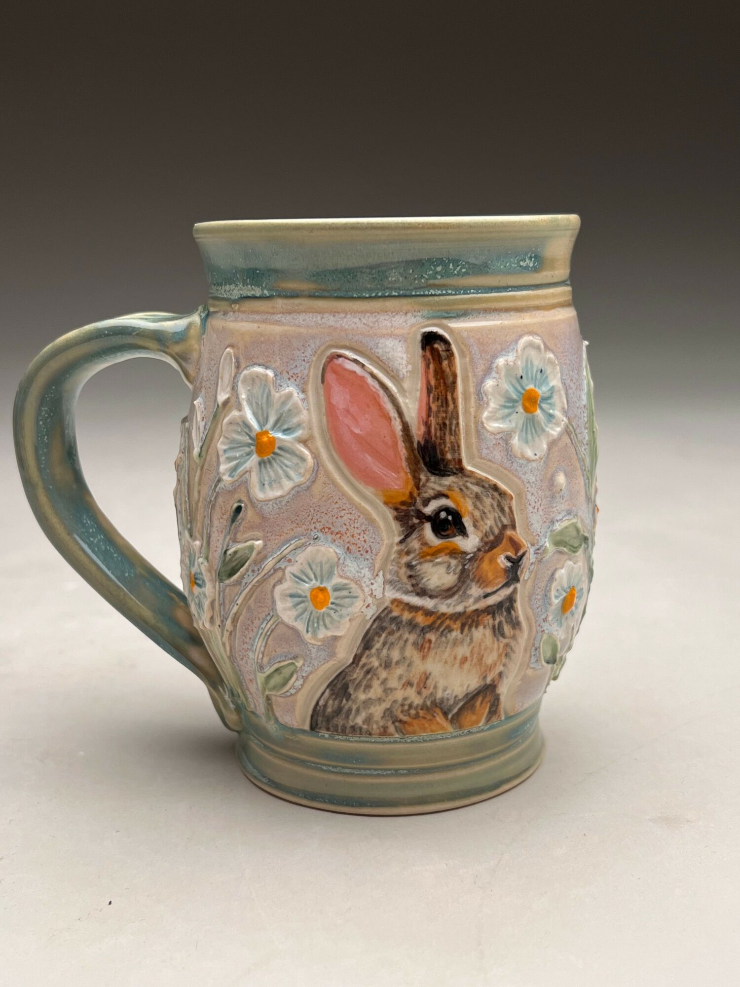 Decorative mug with a rabbit, flowers, and pastel colors, viewed from the side.
