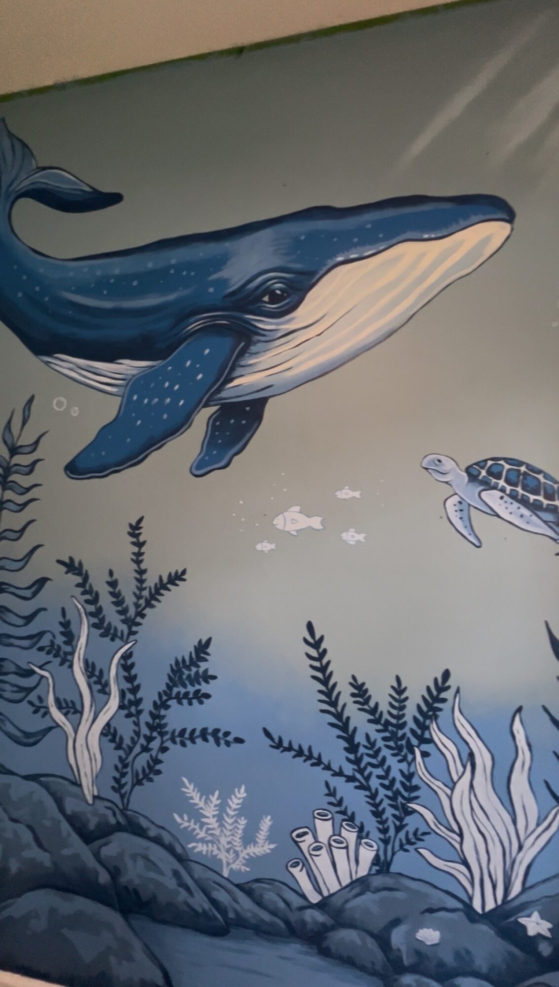 Whale swimming underwater with fish and aquatic plants, in a mural or illustration style.
