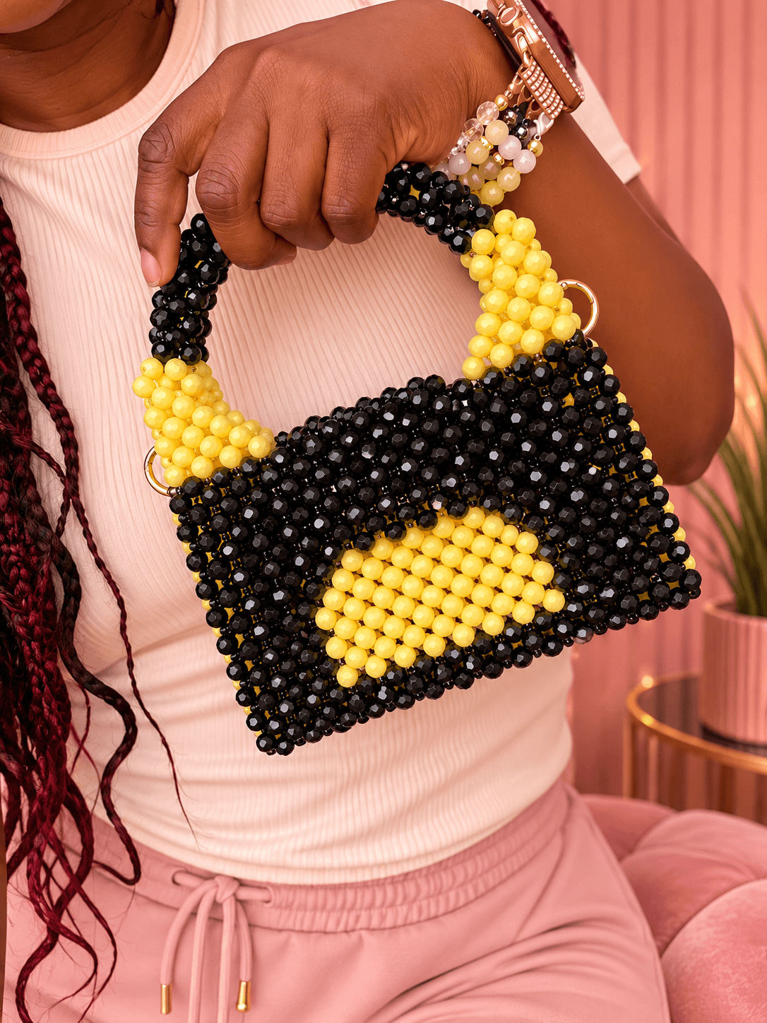 Person holding a beaded handbag with black and yellow beads, against a pink background.