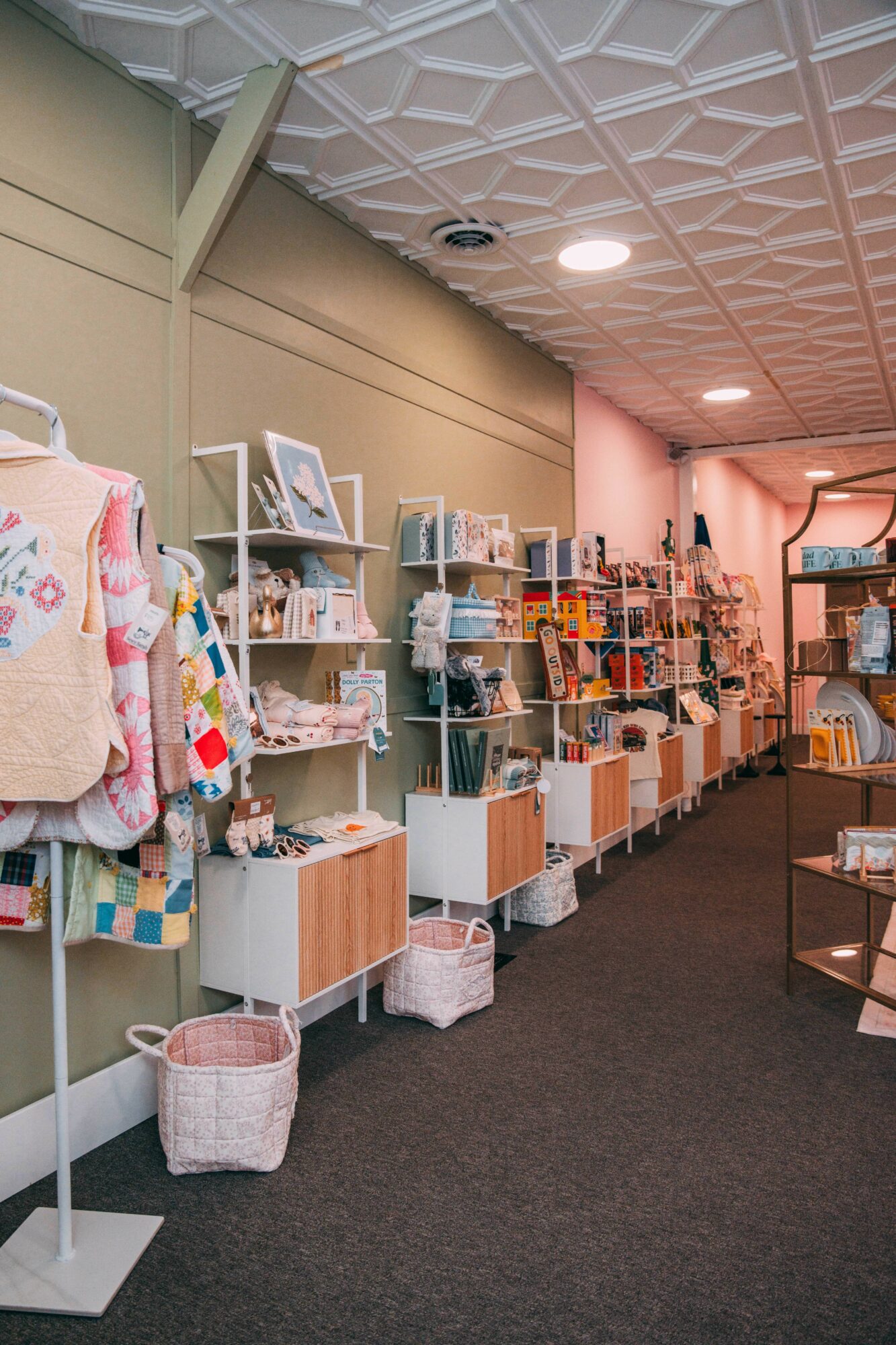 Bookshelves with books and decorative items in a store, with a dark carpeted floor and a patterned ceiling.