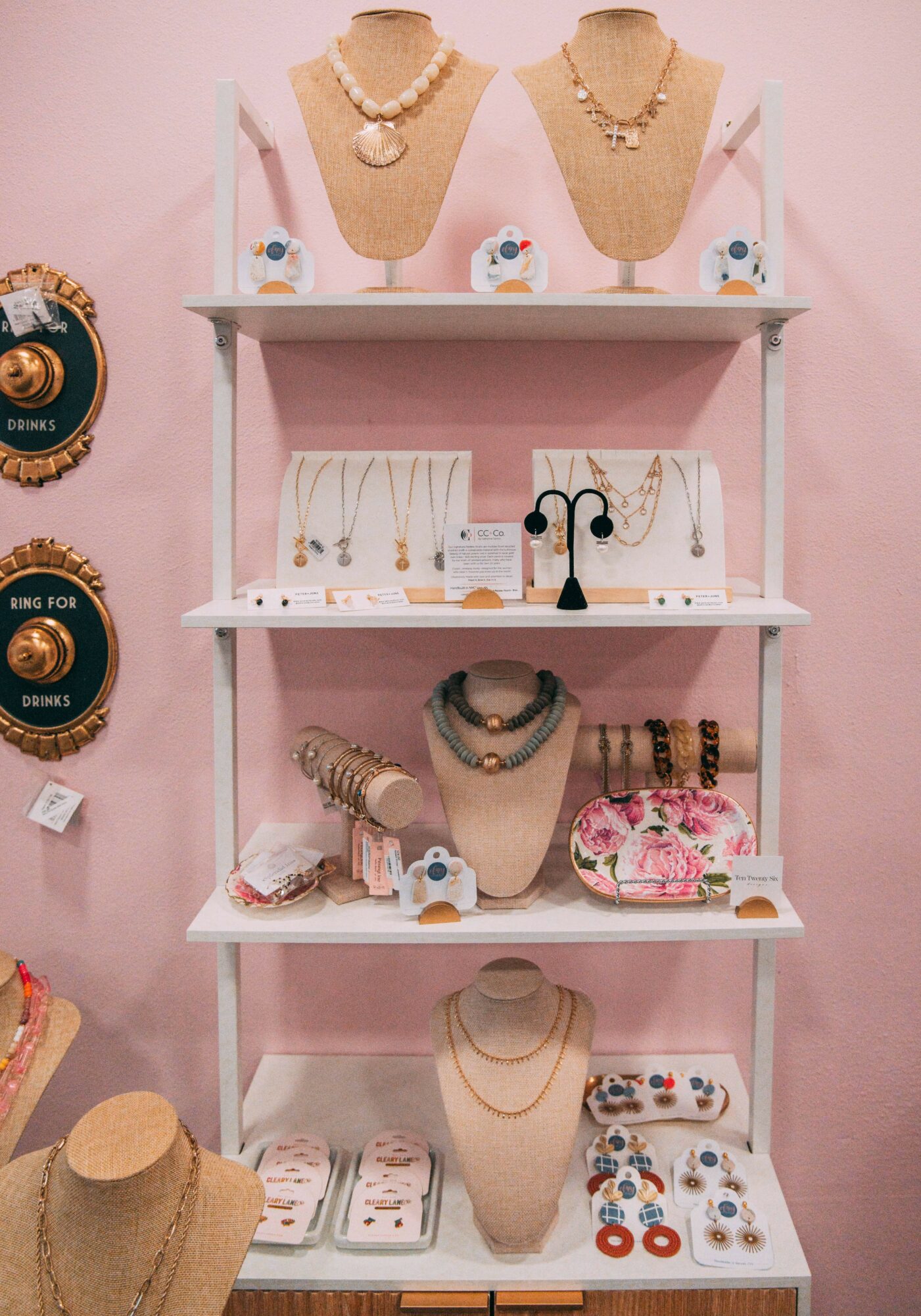 Display of jewelry on mannequins and shelves, with necklaces, earrings, and bracelets, against a pink background.