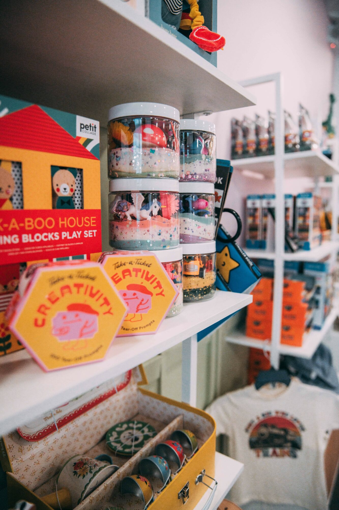 Stacked clear containers with colorful toys and decorations, yellow and pink patches, and shelves with various items in a store.