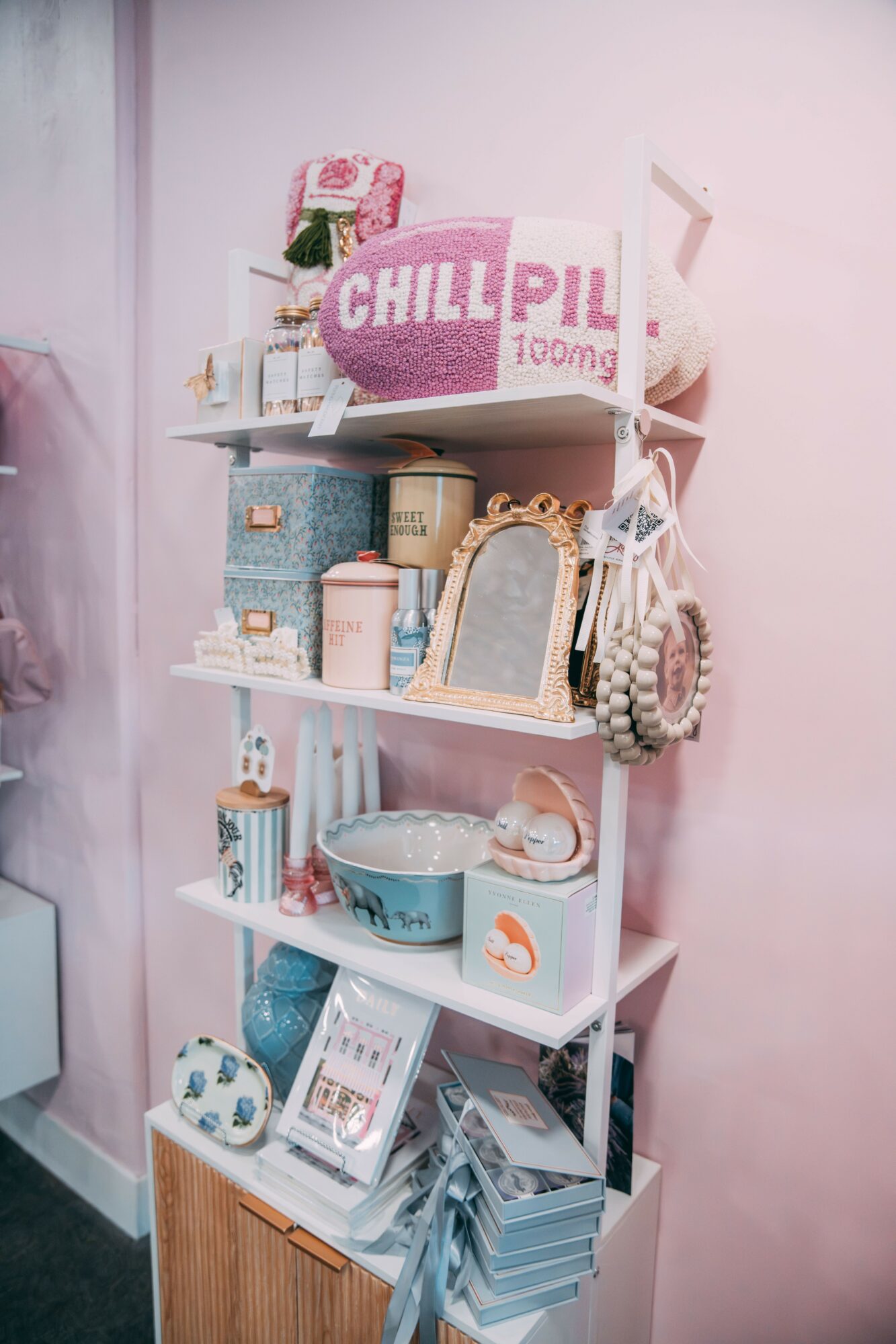 Pink and white shelving unit with various decorative items and books against a pink wall.
